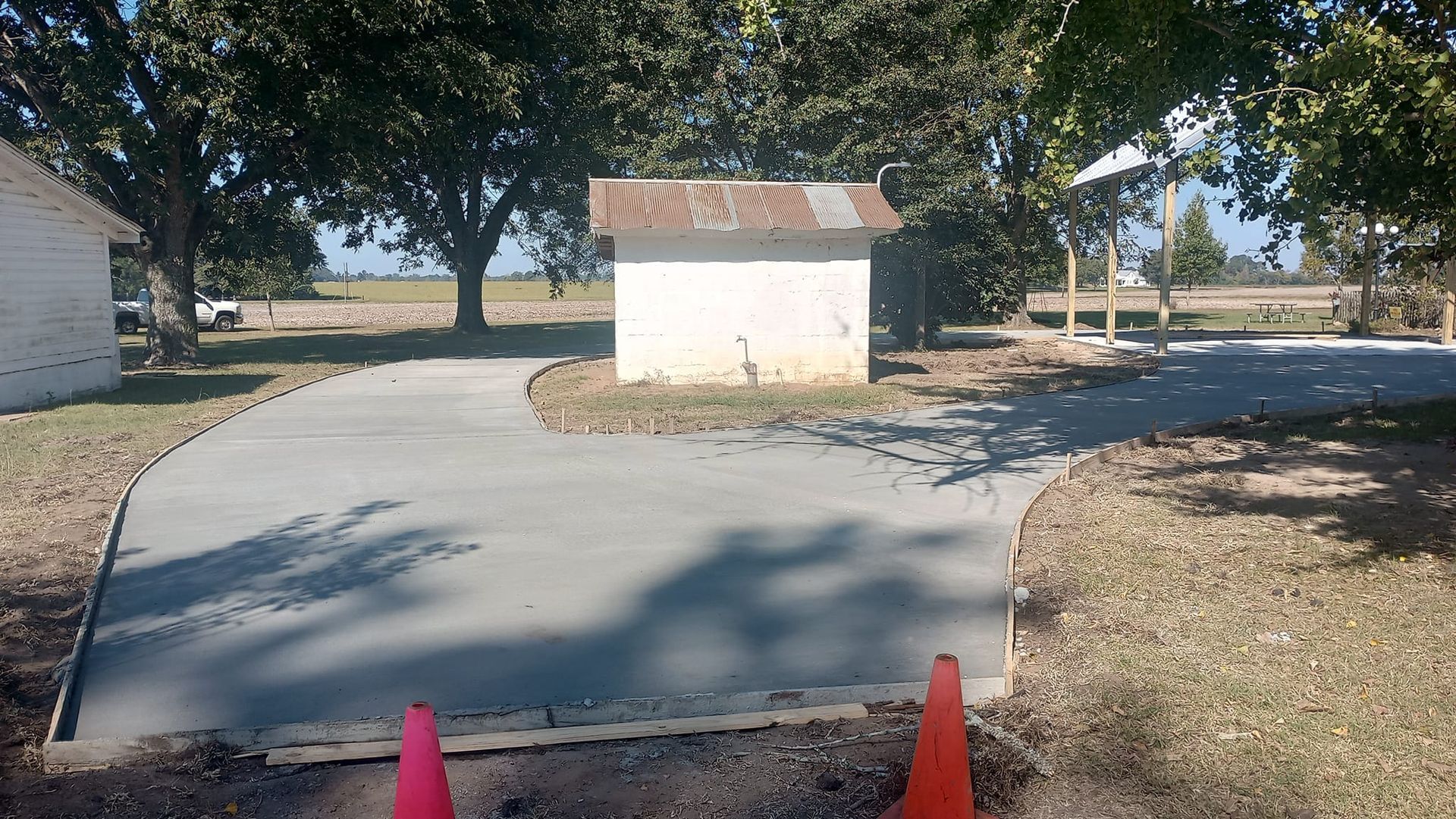 Concrete pathway leading to a small building, orange cones, trees, and a clear sky.