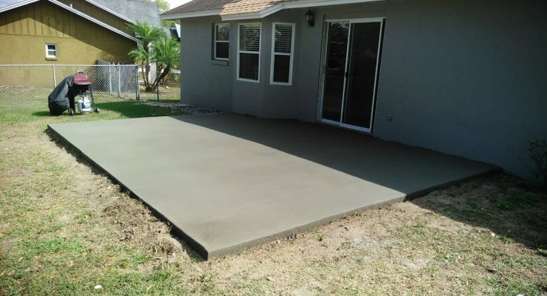 Newly poured concrete patio next to a house with a sliding glass door; a person is in the background.