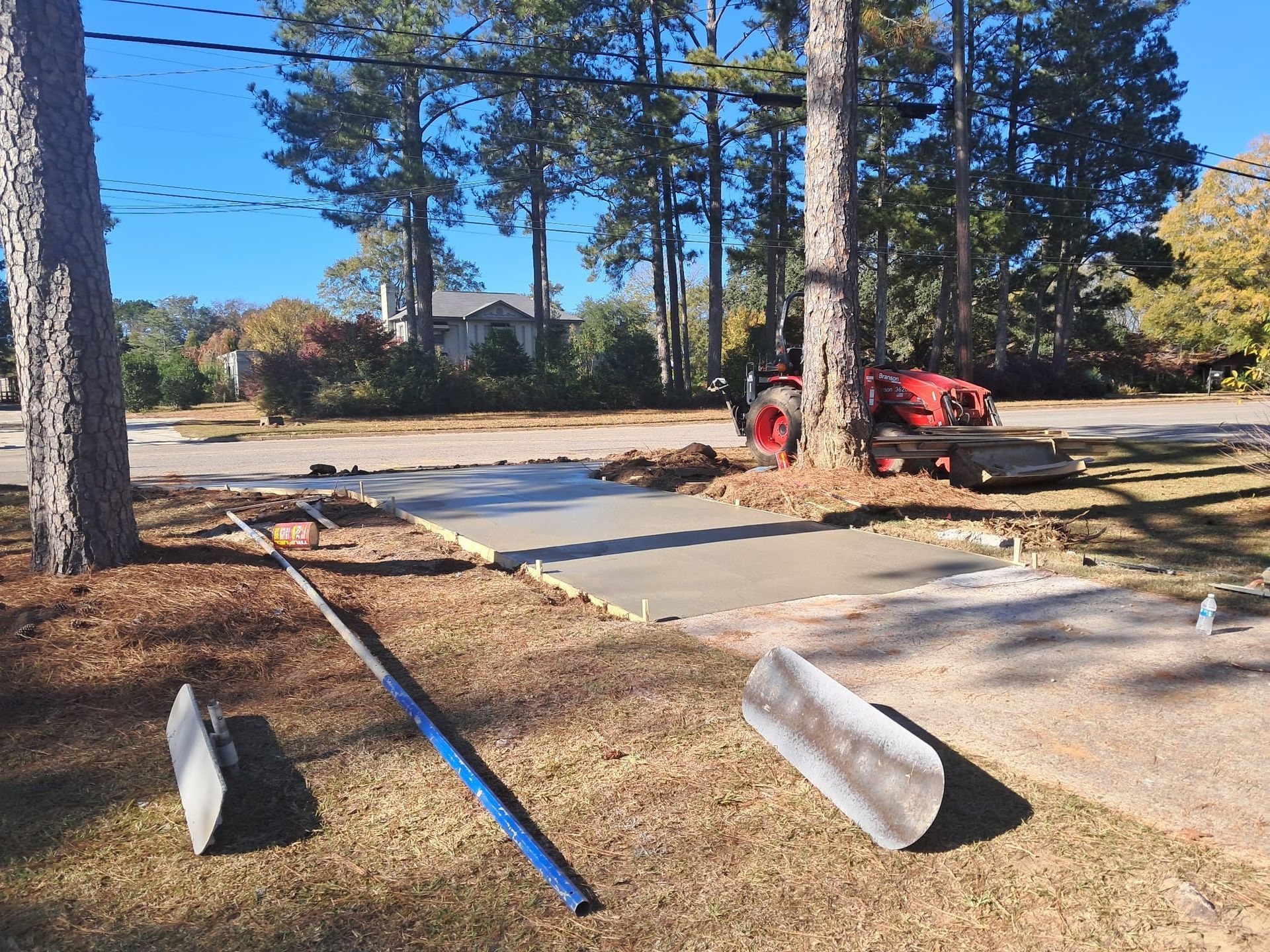 New concrete driveway being poured next to a road, with tools and a tractor present.