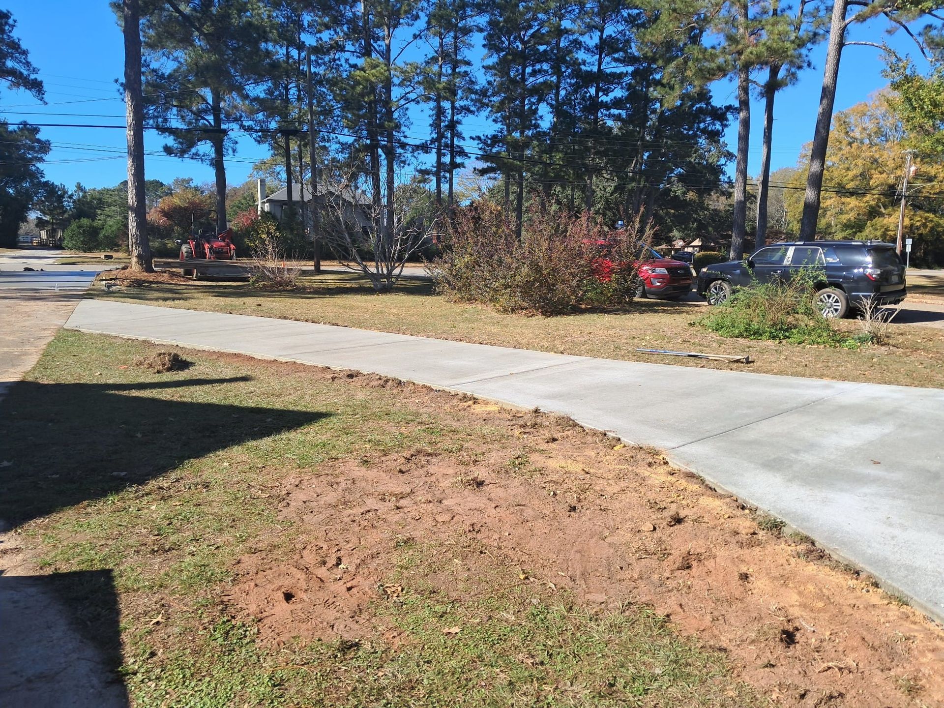 Driveway with grassy area, trees, and parked cars in front of a house on a sunny day.