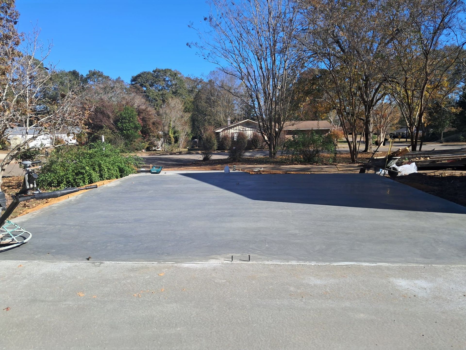Newly poured concrete driveway in front of a house, with surrounding trees and clear blue sky.