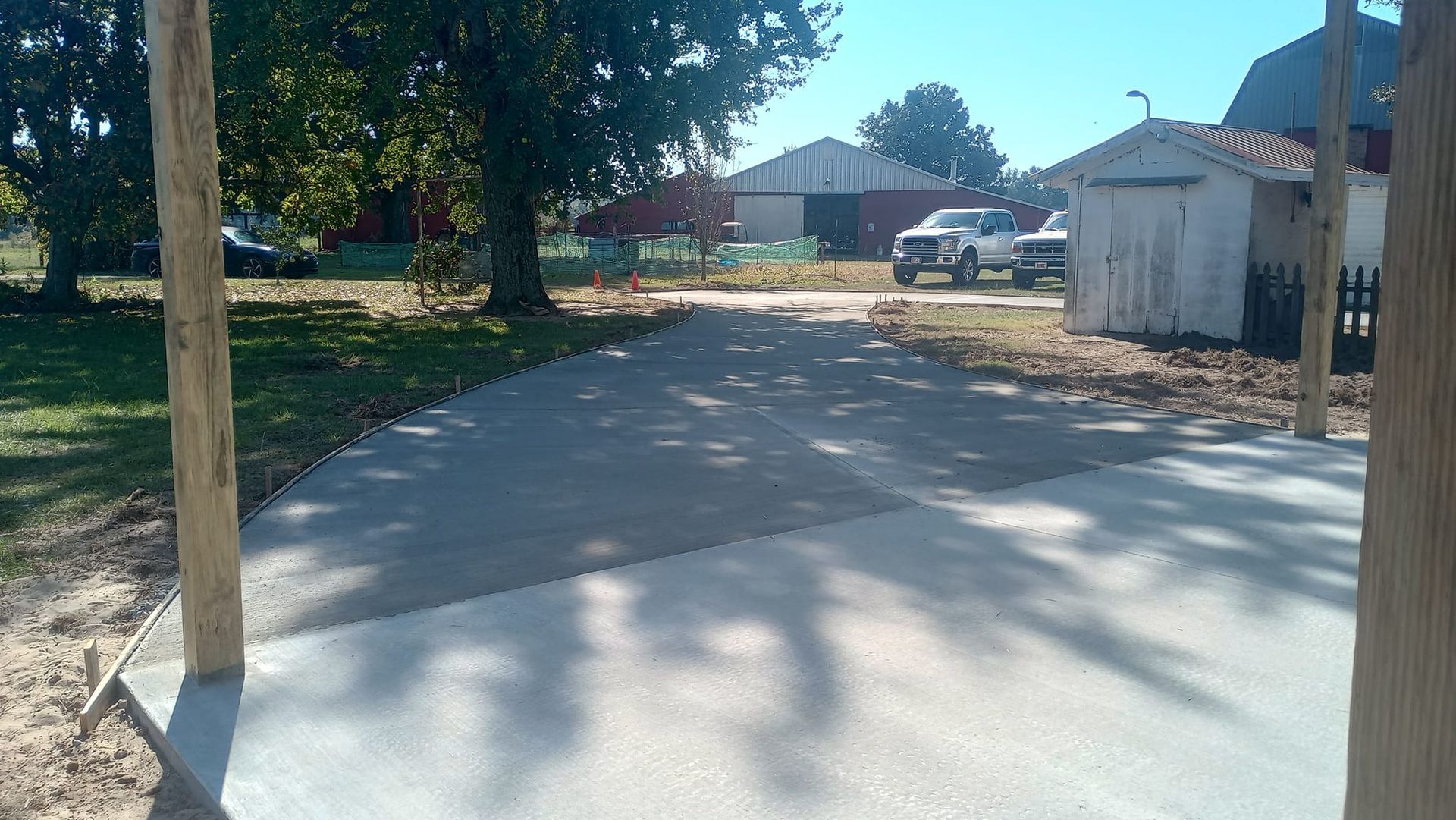 Newly poured concrete driveway leads to buildings and vehicles on a sunny day.