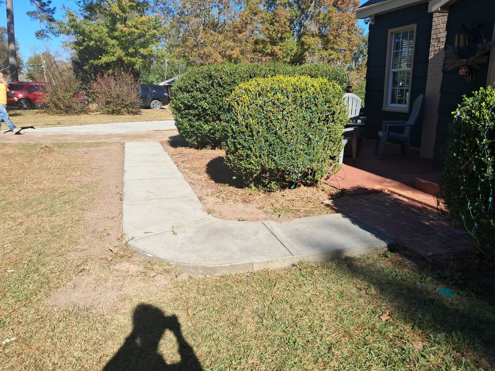 Concrete walkway curving towards a house, with green bushes and grass. Bright, sunny day.