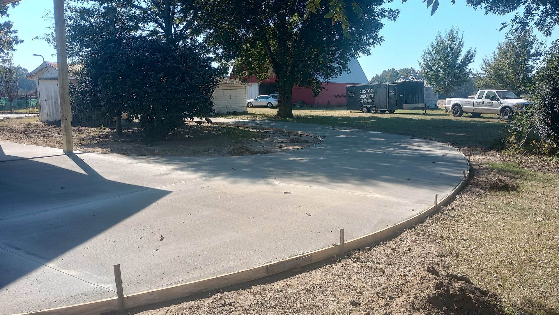 Concrete driveway with wooden forms, in front of trees and a red barn.