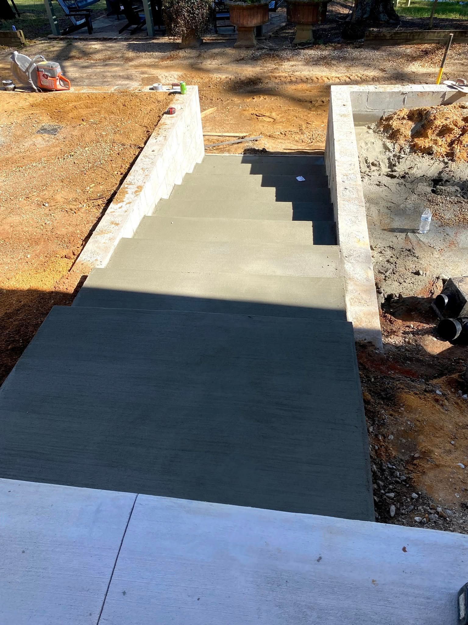 Concrete steps leading up, flanked by retaining walls, under construction.