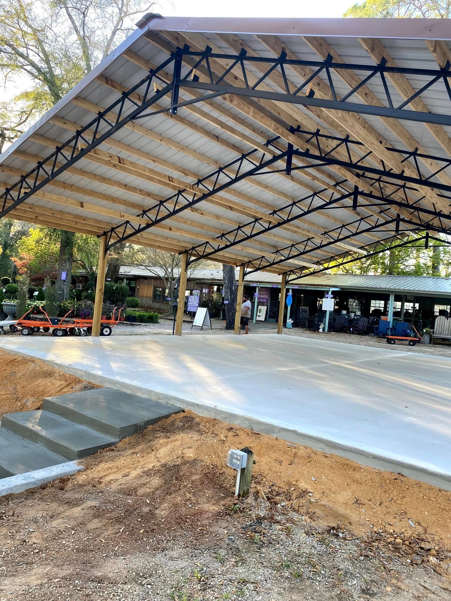 Covered outdoor structure with concrete floor, metal roof, and people.