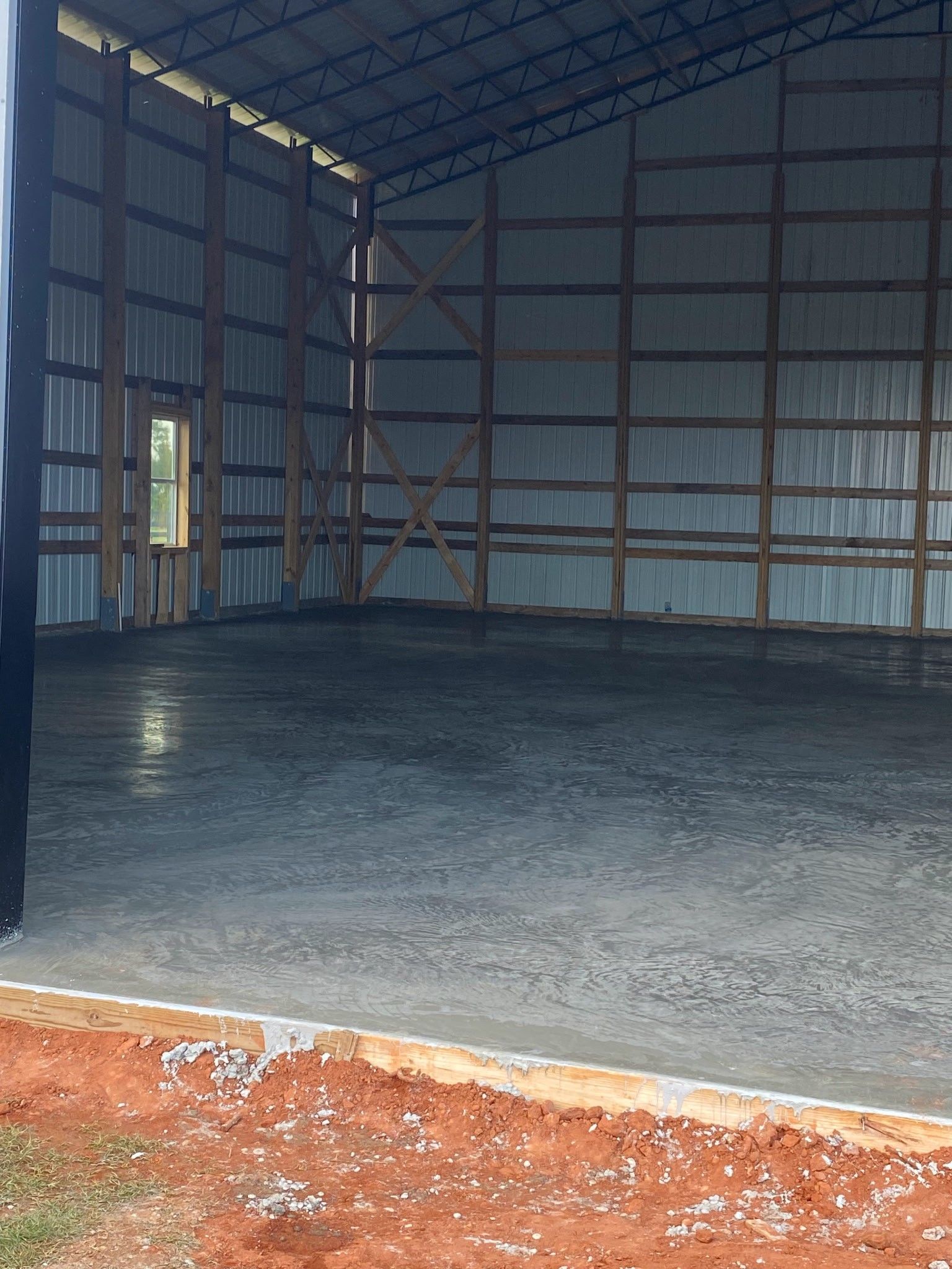 Newly poured concrete slab under a metal roof supported by wooden posts. Person standing in the background.