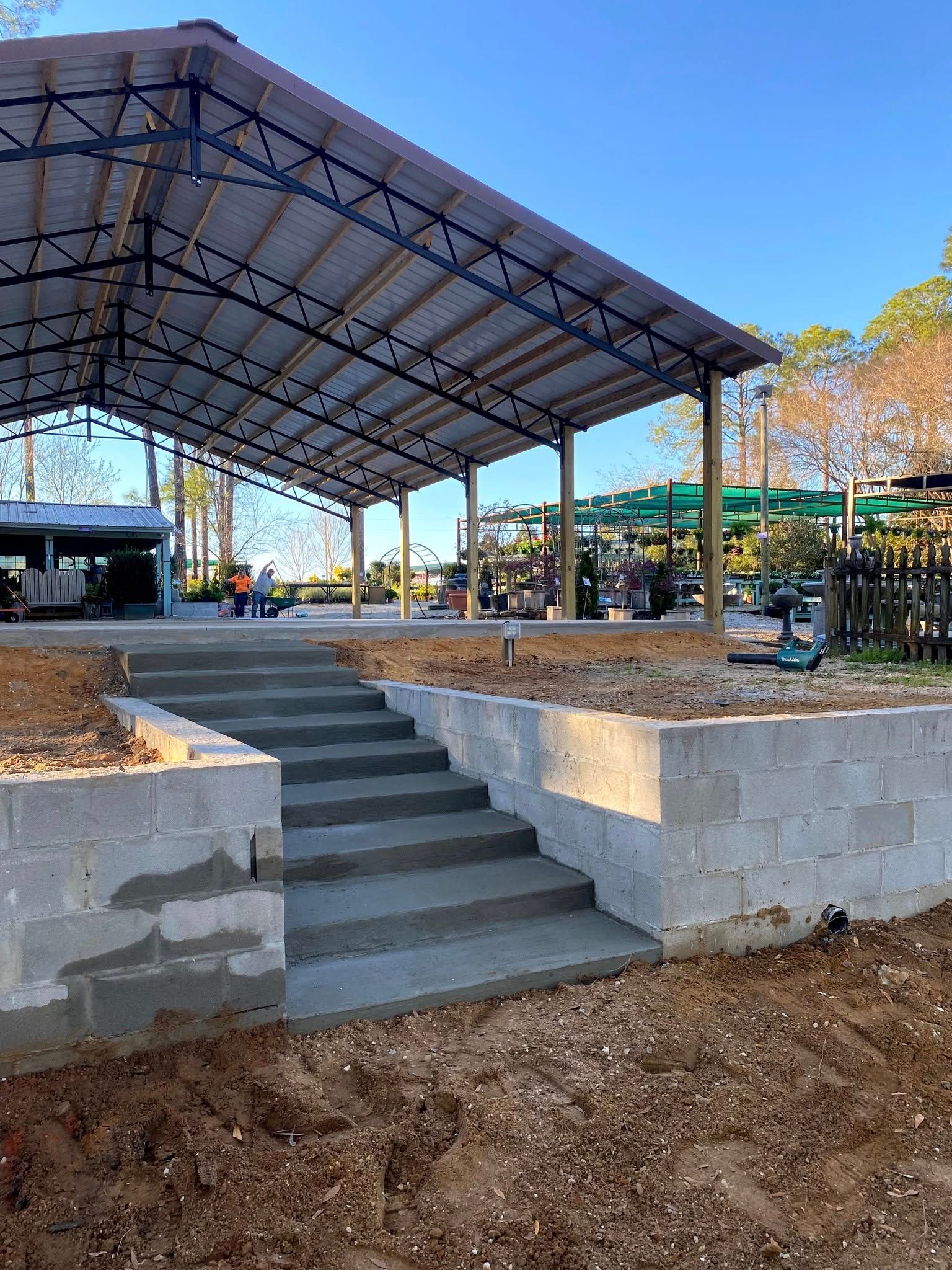 Concrete steps leading up to an open-air building with metal roof. Construction in progress.