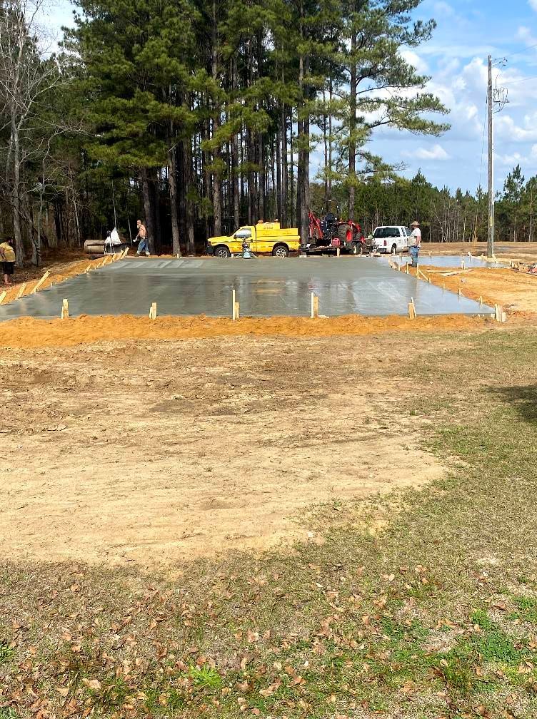 Freshly poured concrete slab with construction vehicles and workers on a rural site.