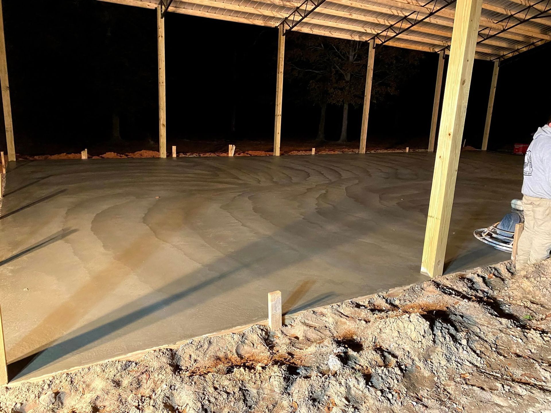 Newly poured concrete floor under a wooden structure at night.