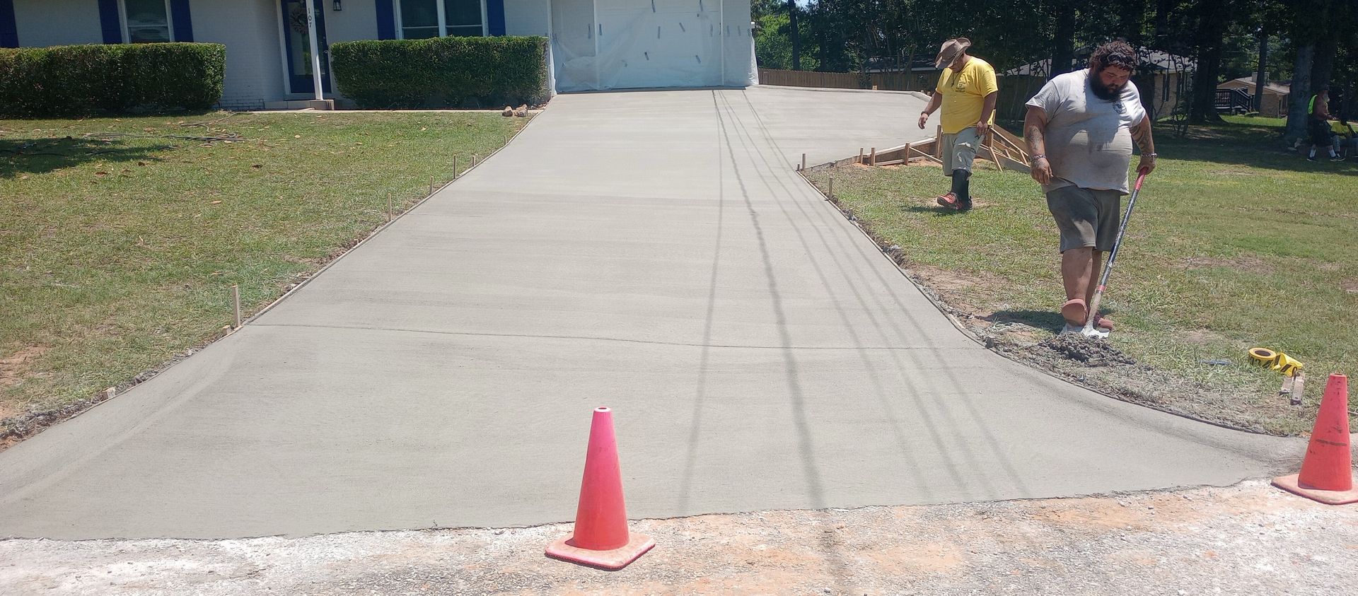Two men working on a newly poured concrete driveway with traffic cones.
