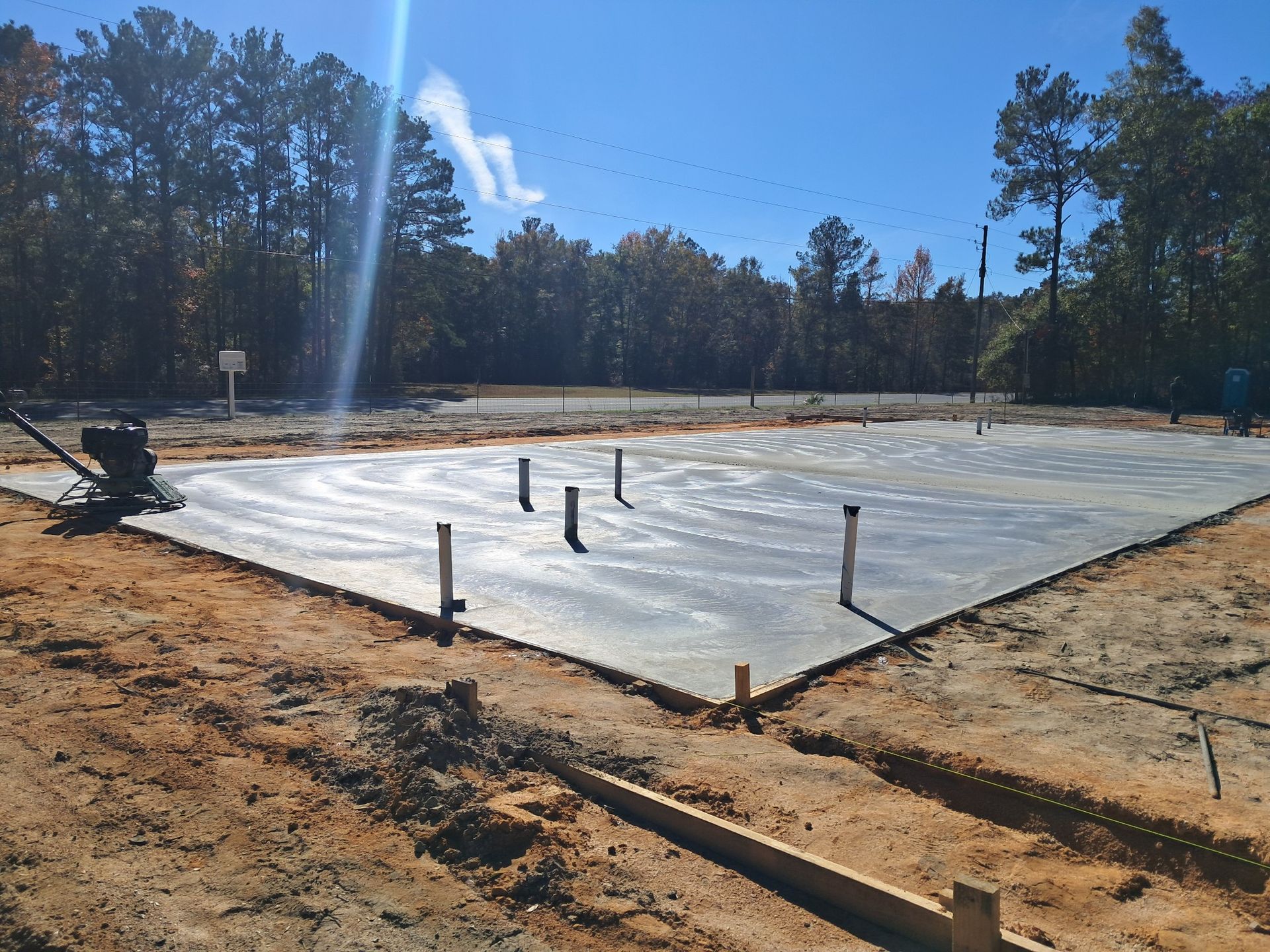 Newly poured concrete foundation with plumbing pipes, outdoors.
