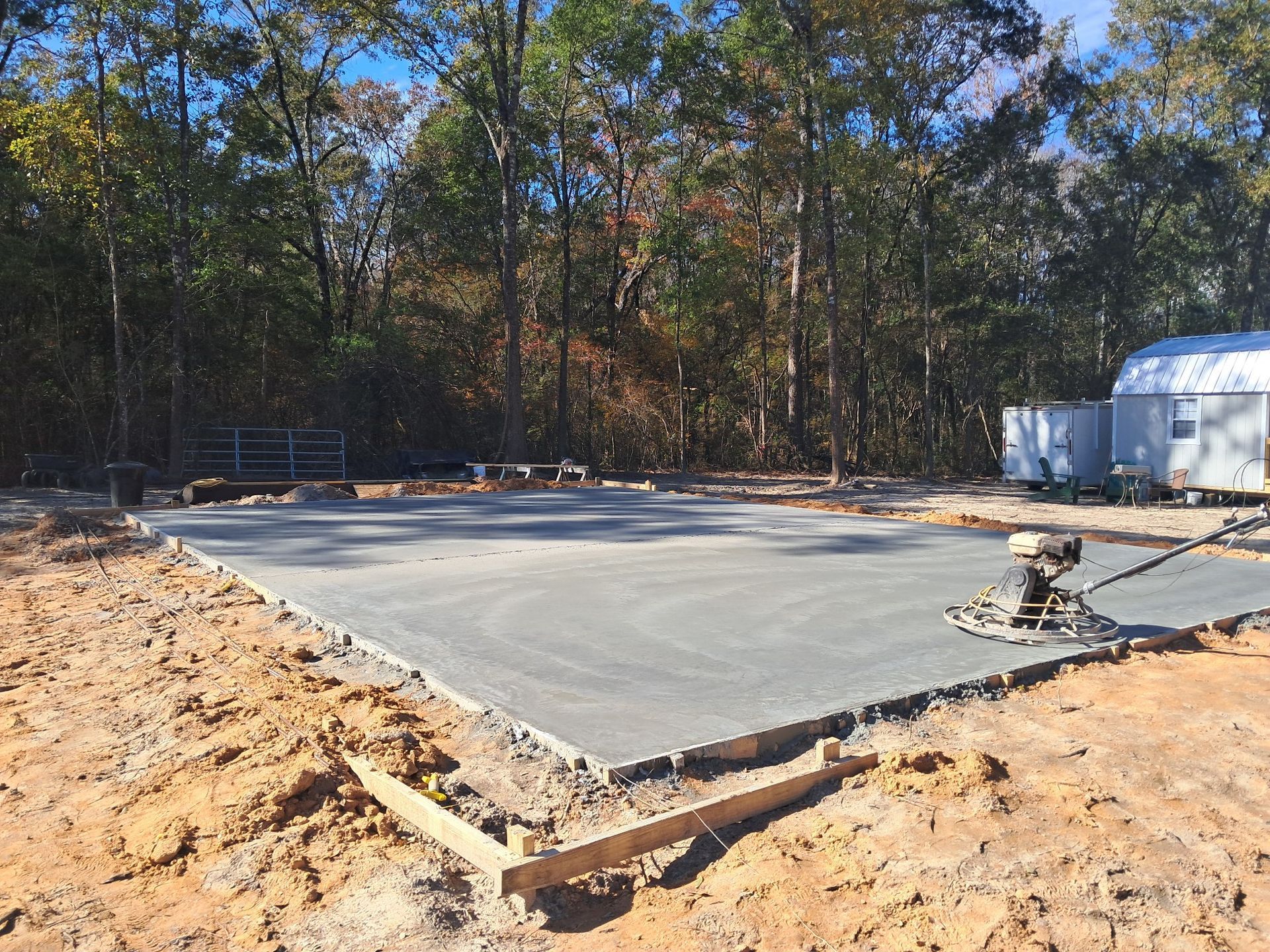 Freshly poured concrete foundation; construction site with surrounding dirt and trees.