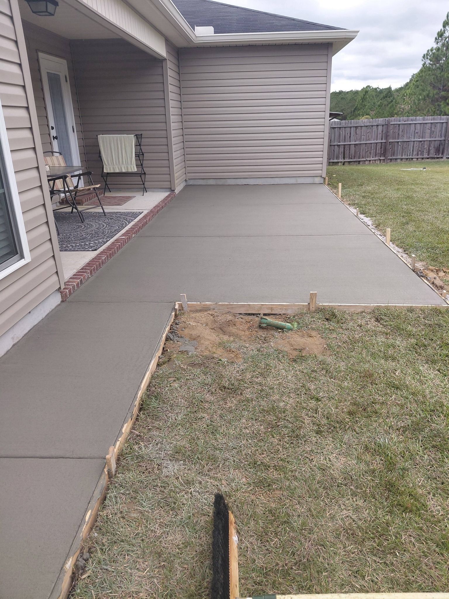 Newly poured concrete patio next to a house with grass and a fence in the background.