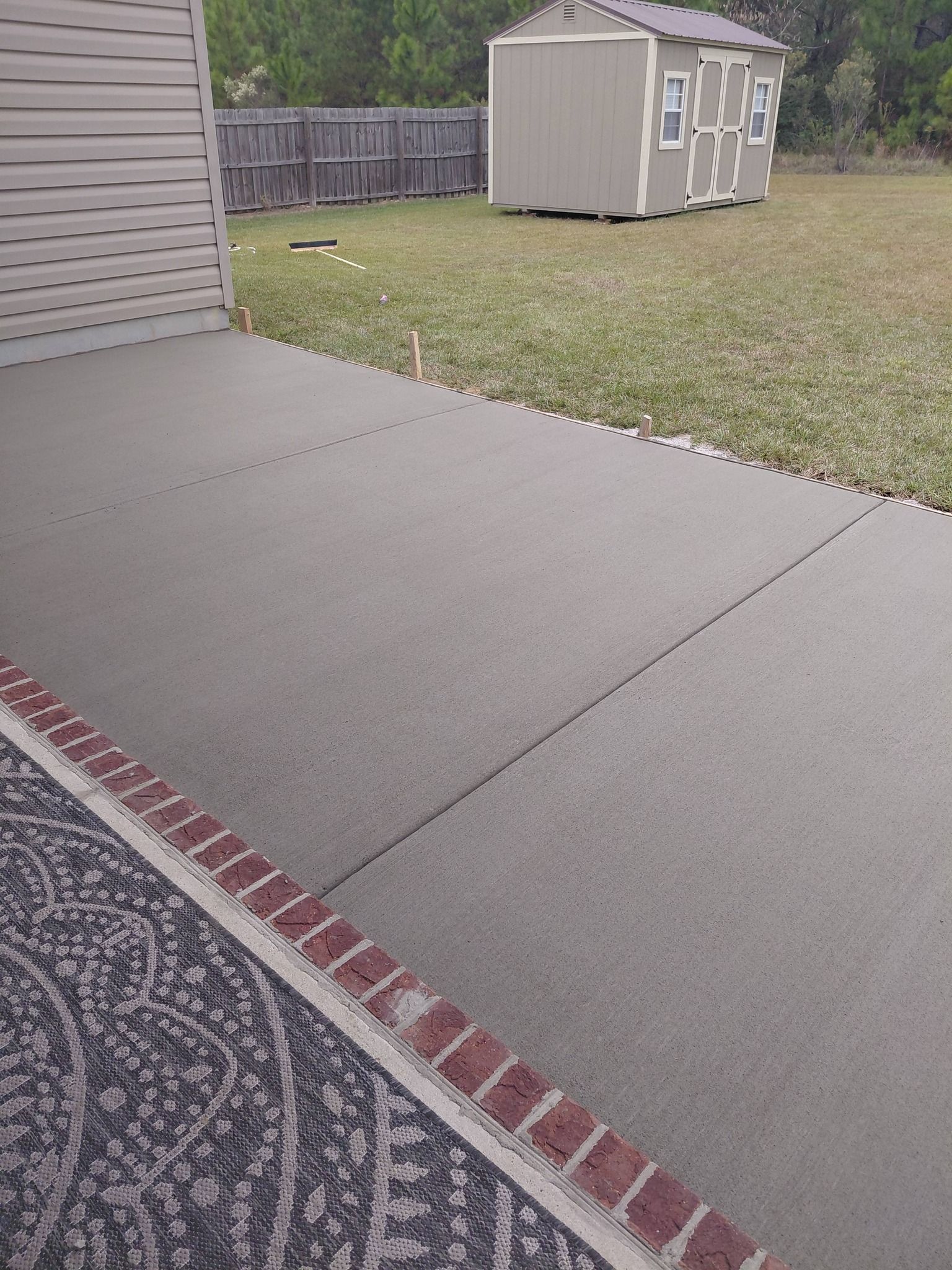 Concrete patio with brick border, leading to a yard with a shed.