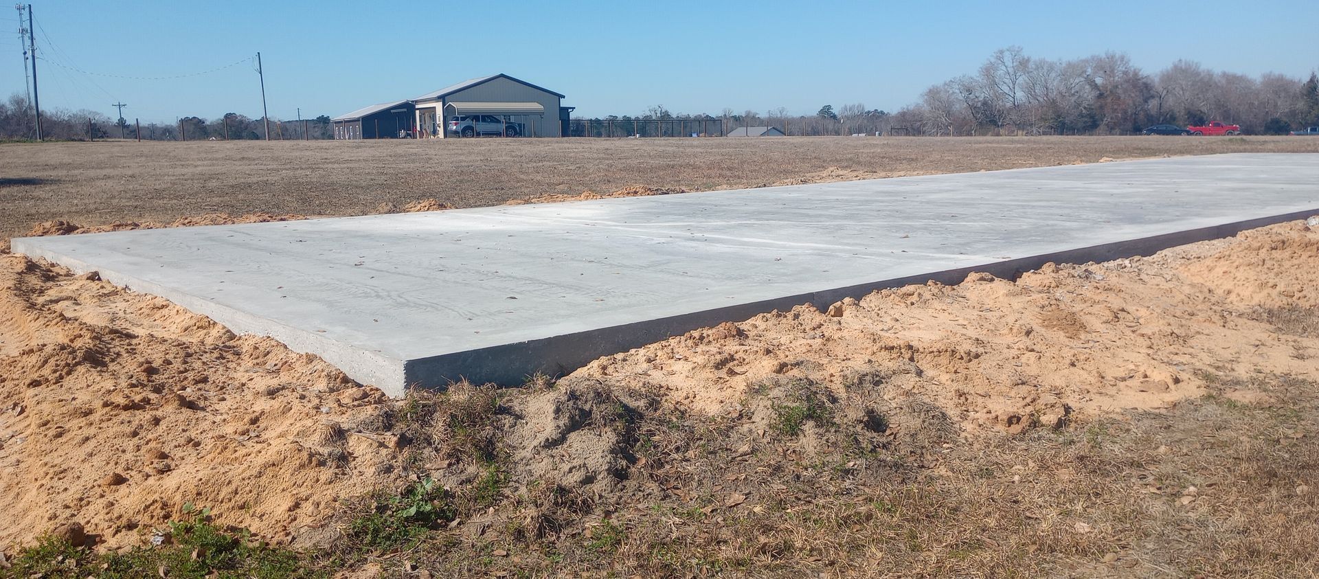 A concrete slab on a construction site with a building in the background. Brown dirt surrounds the slab.