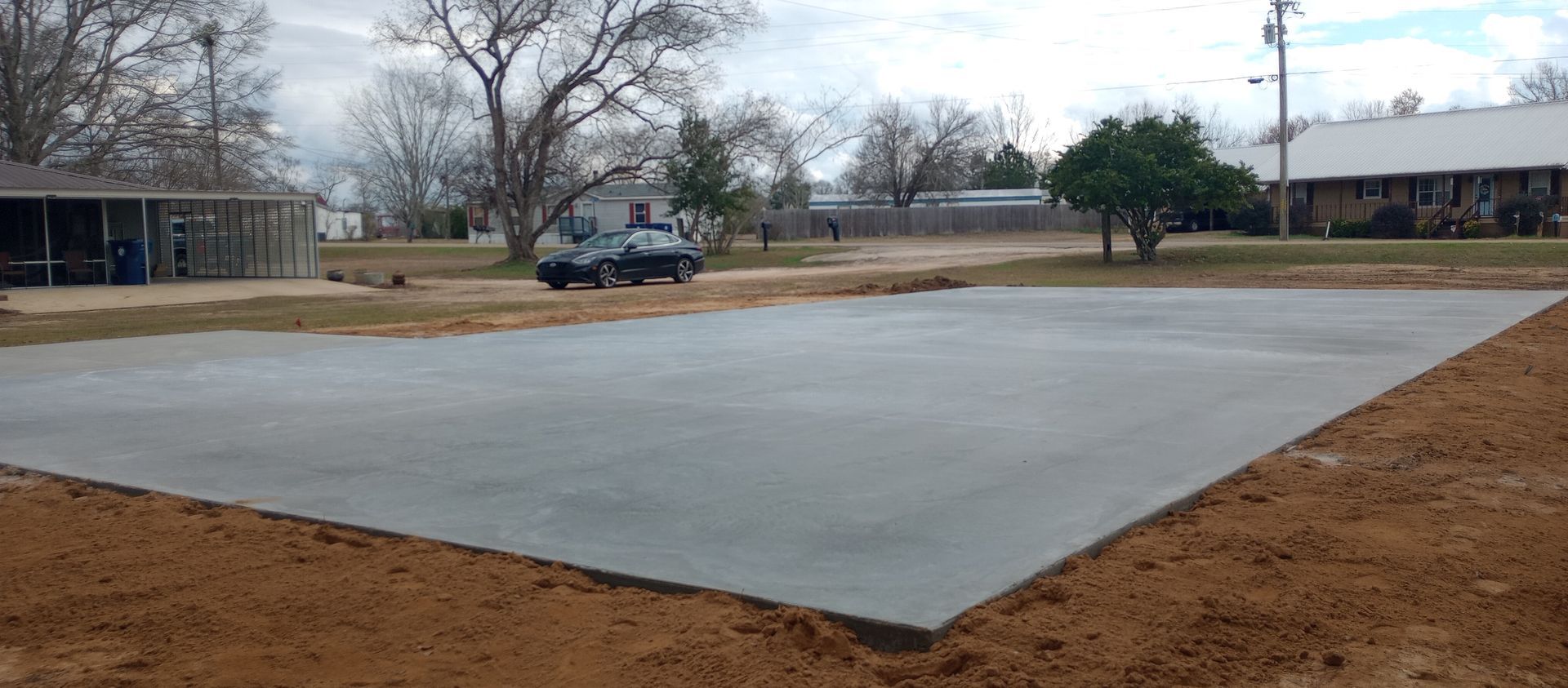 A rectangular concrete slab in an open, grassy area with trees and buildings in the background.