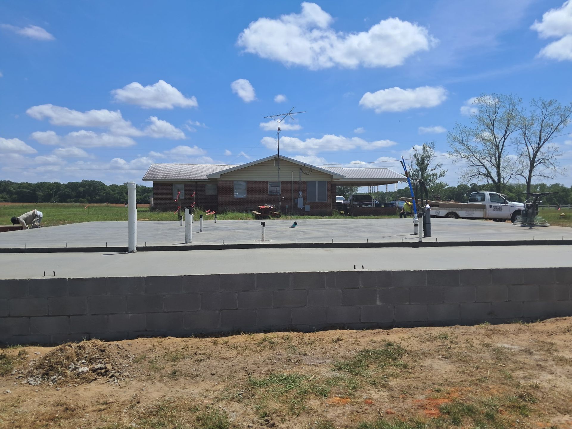 House with new concrete driveway and retaining wall on a sunny day. White pickup truck parked.