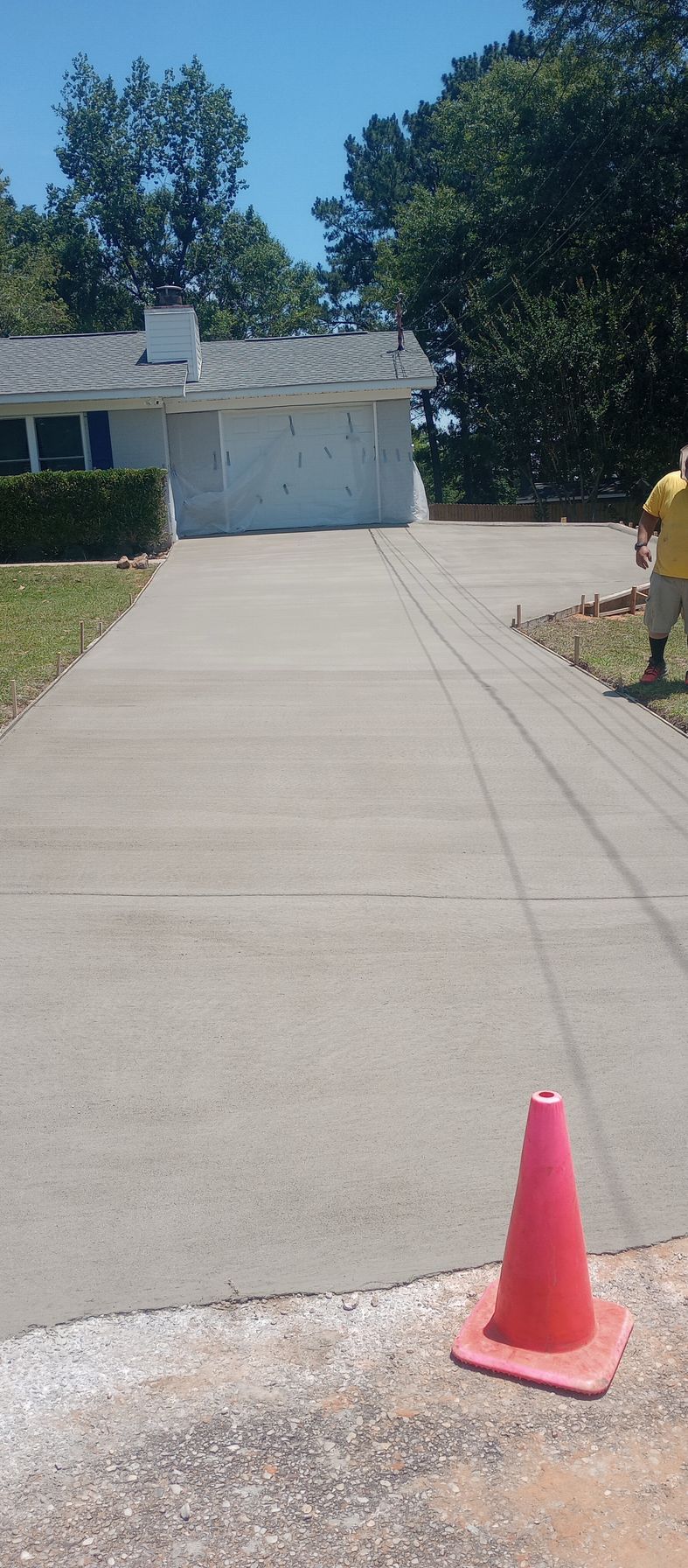 A newly paved concrete driveway with a traffic cone; a house in the background and a worker on the right.