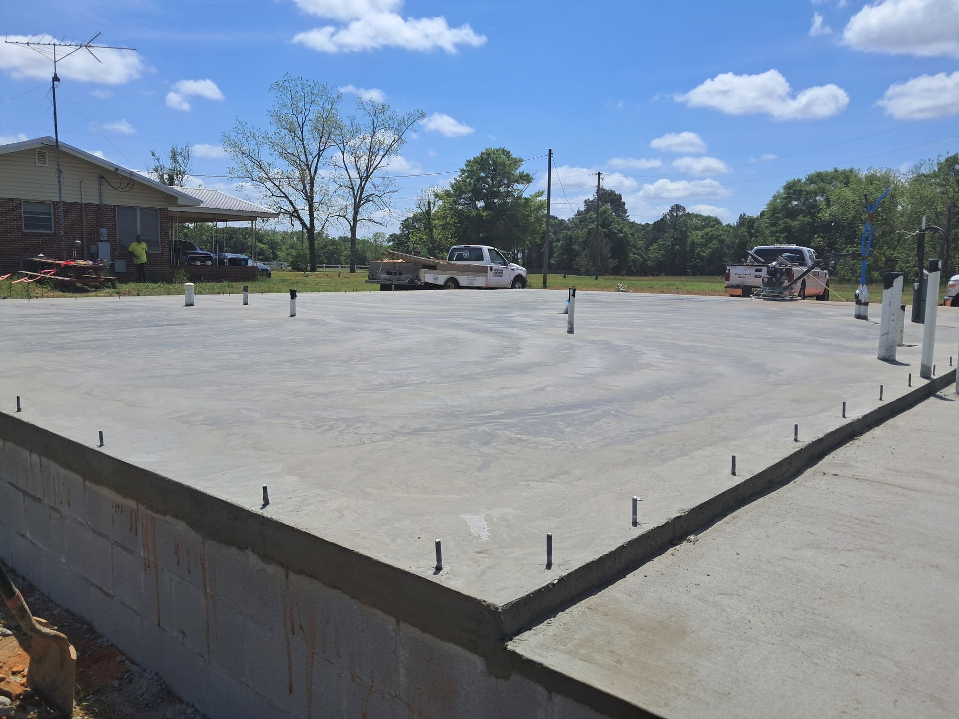 Newly poured concrete foundation with protruding pipes, outdoors, daytime.