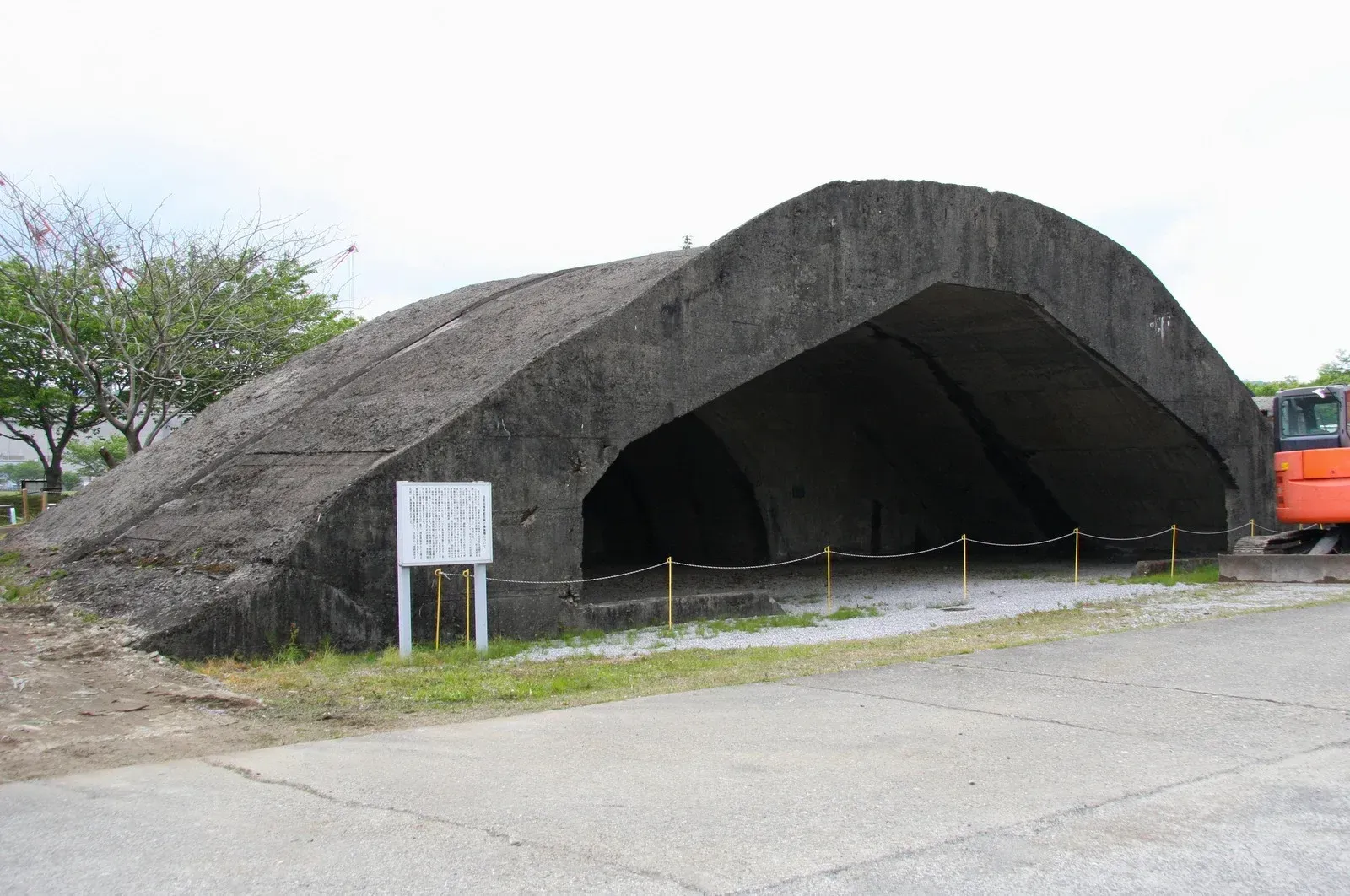 Large concrete arched structure, possibly a bunker, in an outdoor setting with a sign and excavator.