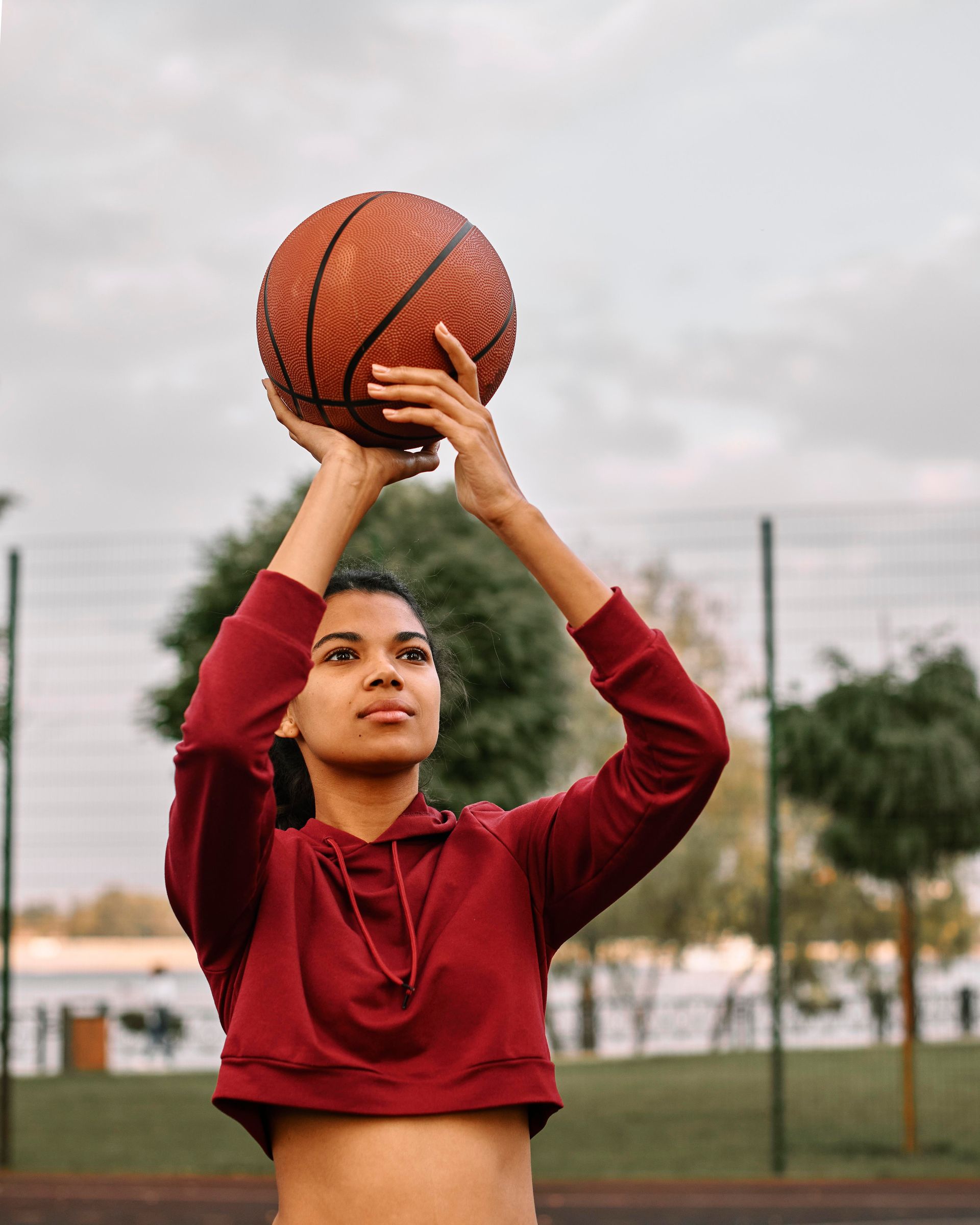 Mulher com capuz vermelho prestes a arremessar uma bola de basquete ao ar livre.
