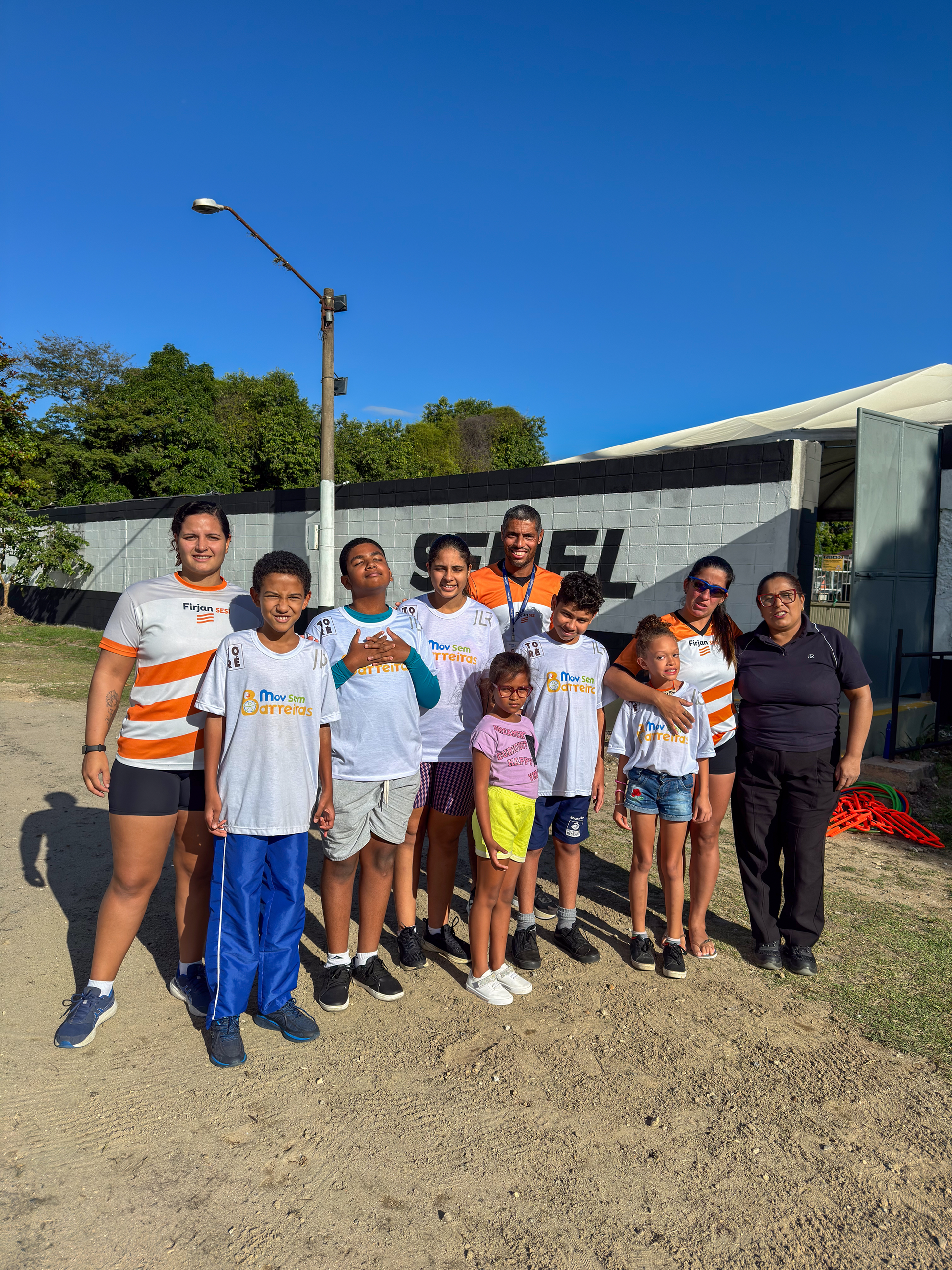 Grupo de pessoas, crianças e adultos, em frente a um prédio com a inscrição