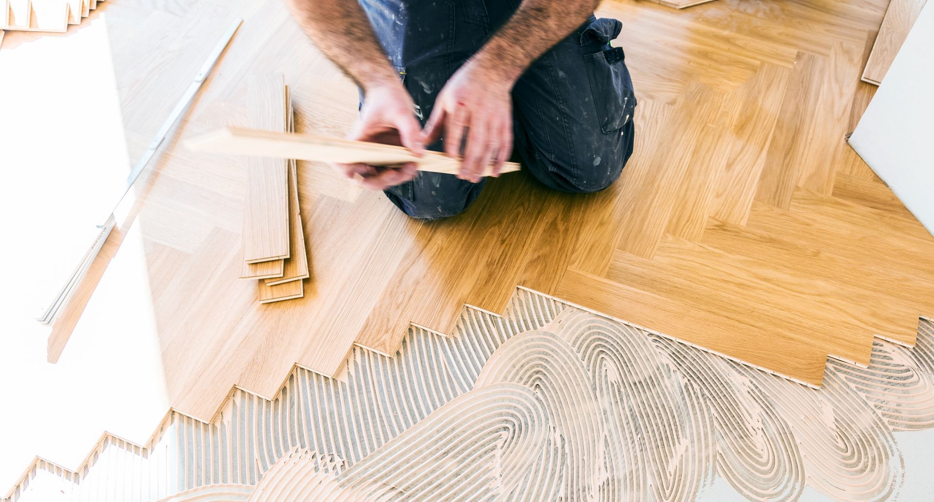 A man is kneeling on the floor while installing a wooden floor.