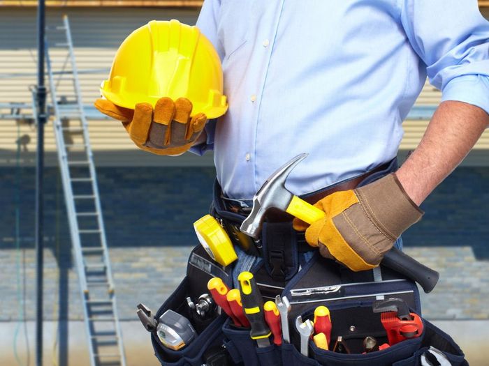 A construction worker is holding a hard hat and a tool belt.