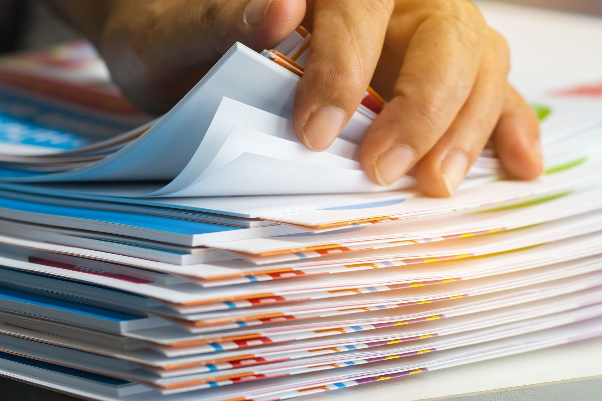 Hand flipping through a thick stack of colorful documents on a desk