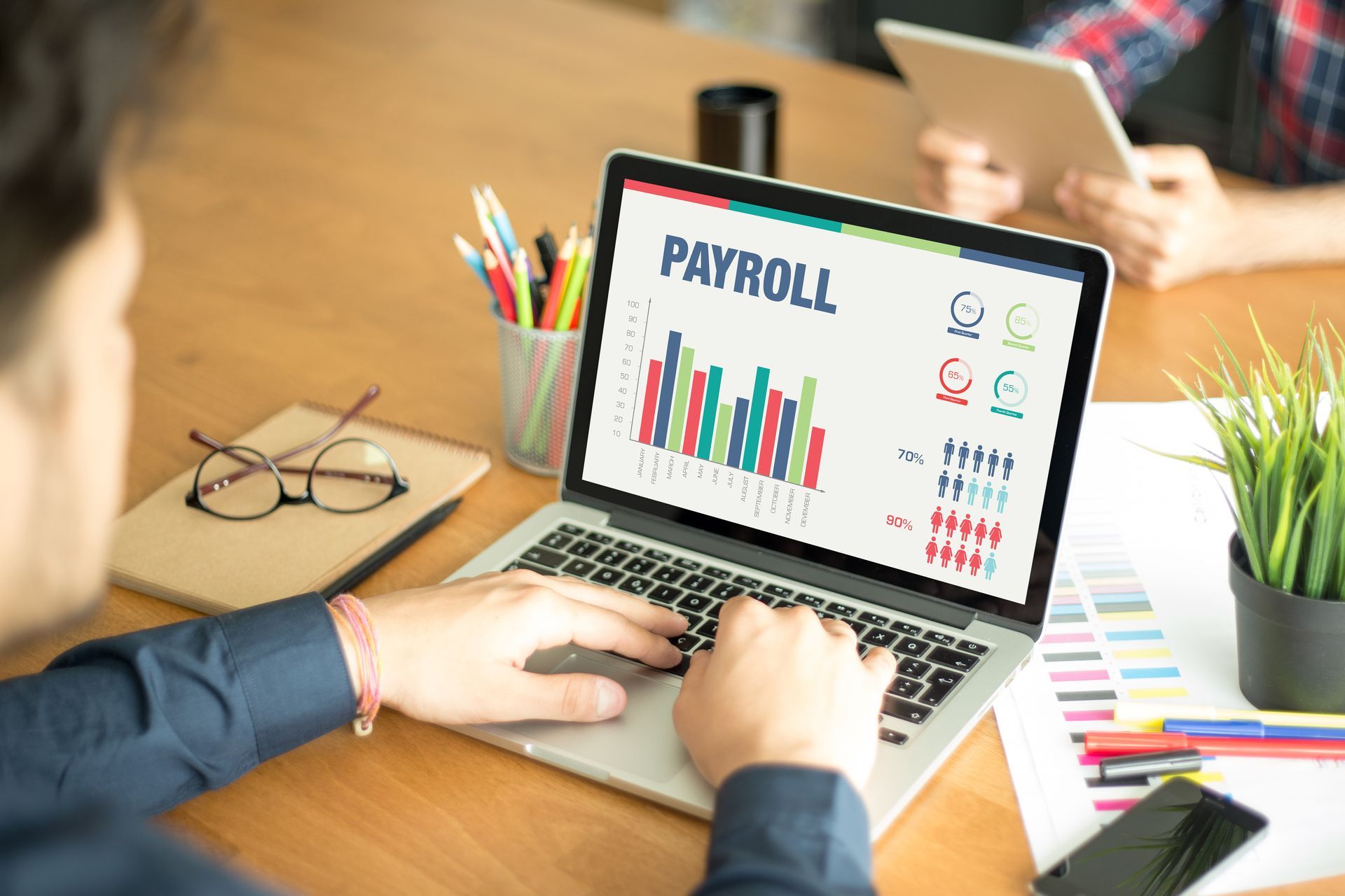 Hands using a laptop showing a payroll dashboard with charts on a desk in an office setting