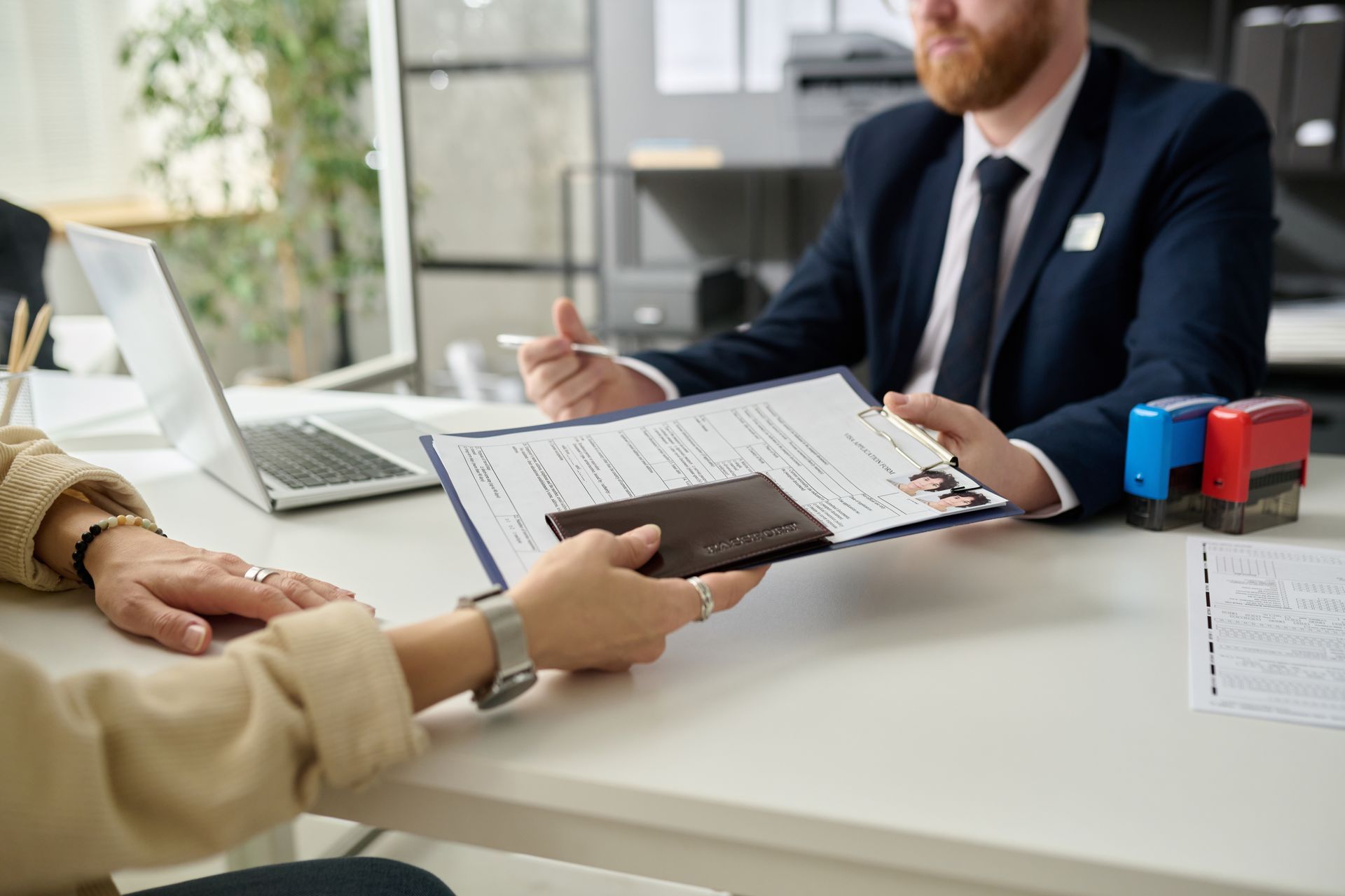 Person hands a card at a business desk while a clerk reviews paperwork in an office.