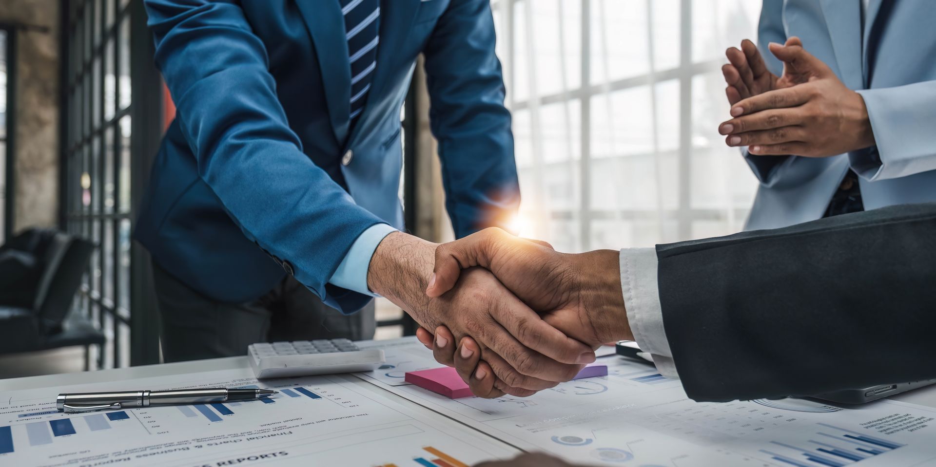 Businesspeople shaking hands over charts in a bright office