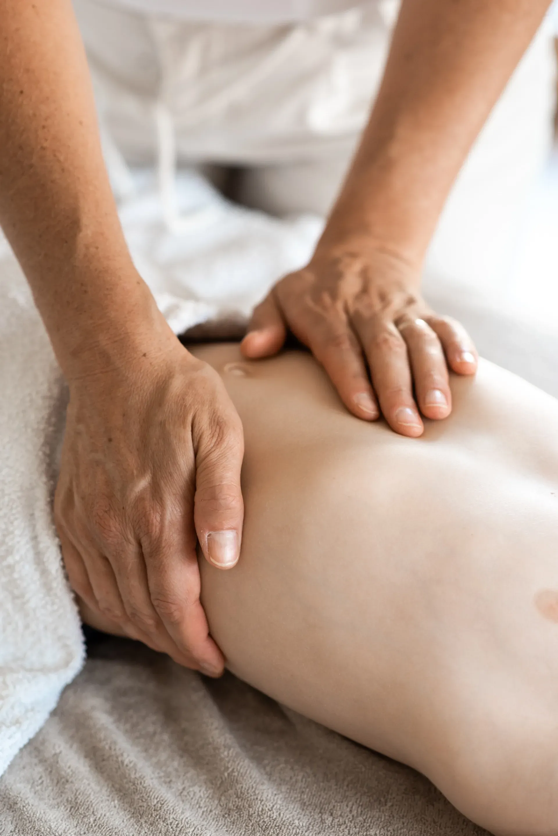 Hände massieren den Bauch einer Person auf einem Massagetisch; die Person trägt ein weißes Handtuch.
