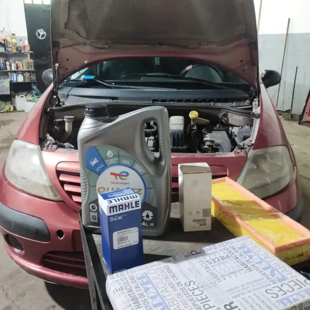 Coche en revisión; cambio de aceite y filtro. Compartimento del motor abierto, coche rojo.