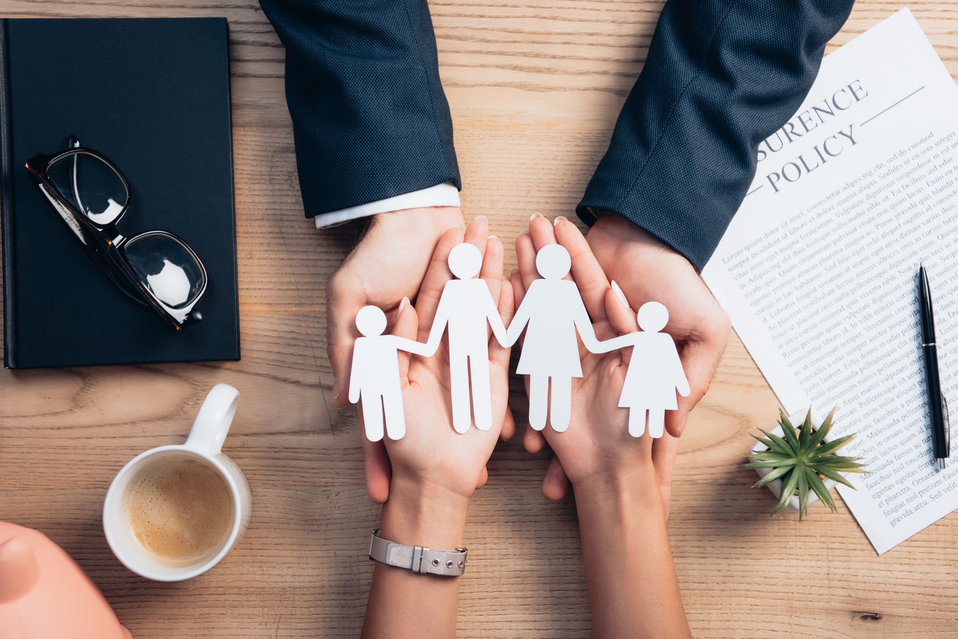 Hands holding paper family cutout over desk with insurance policy and documents.