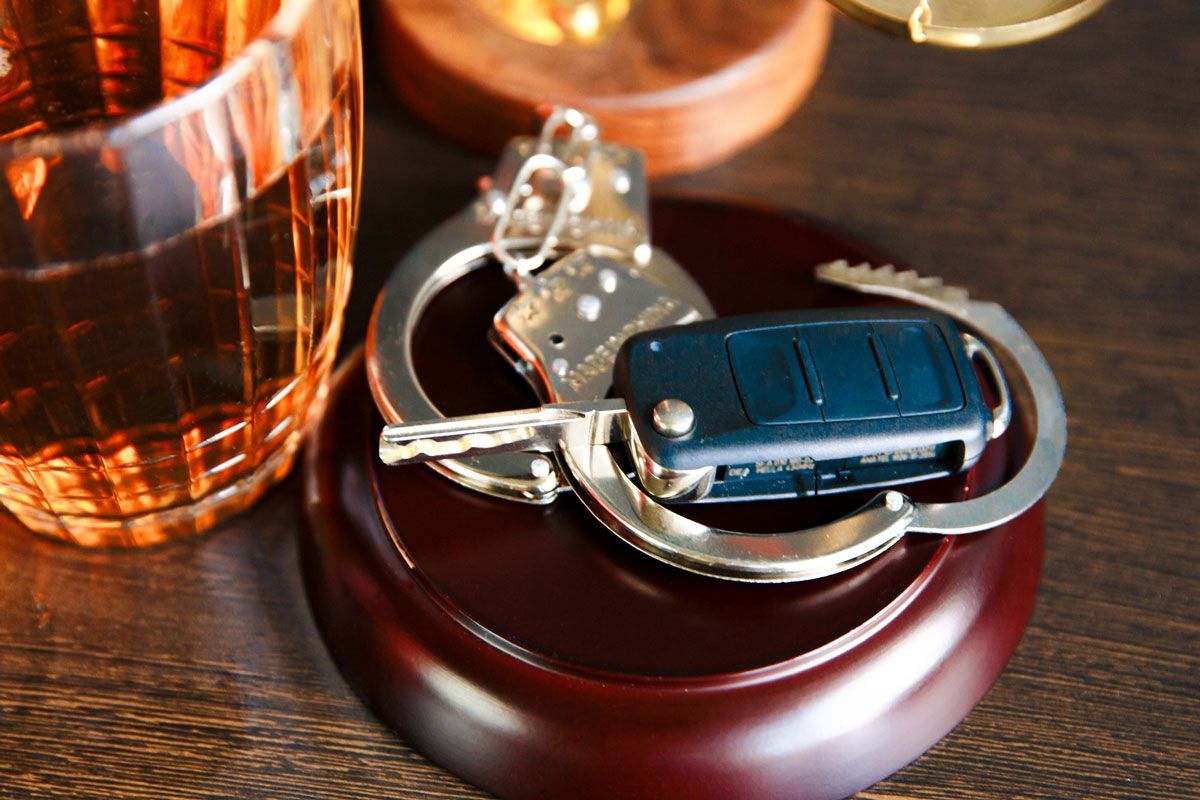 Handcuffs, car key, and drink on a wooden surface, suggesting impaired driving.