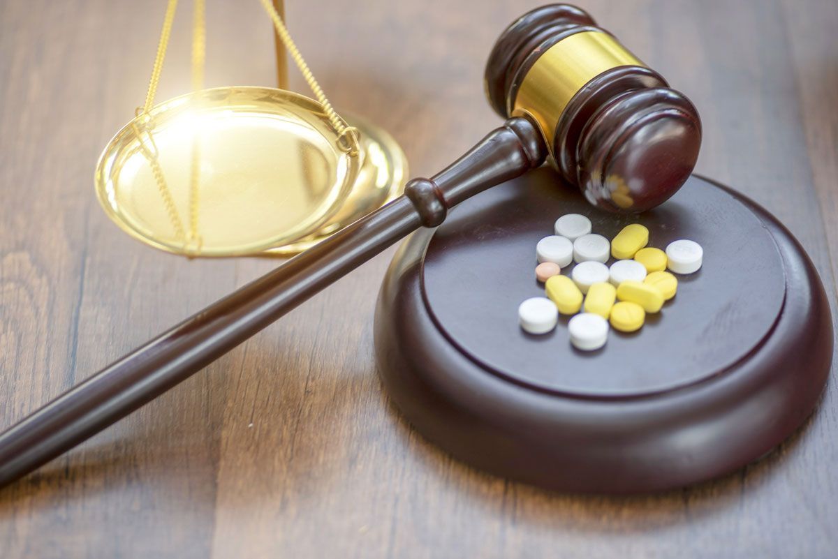 Gavel and scales of justice with pills on a wooden stand, symbolizing legal or medical decision.