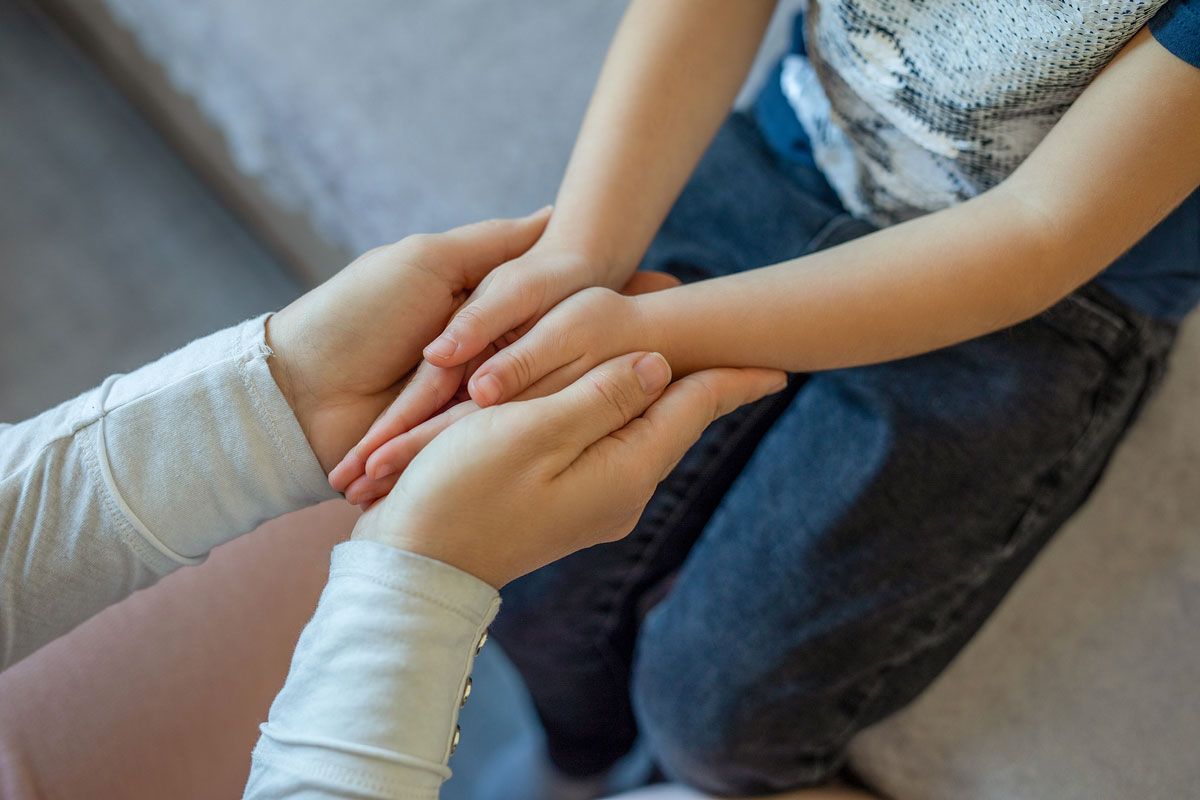 Adult's hands gently hold a child's hands, offering comfort and support.
