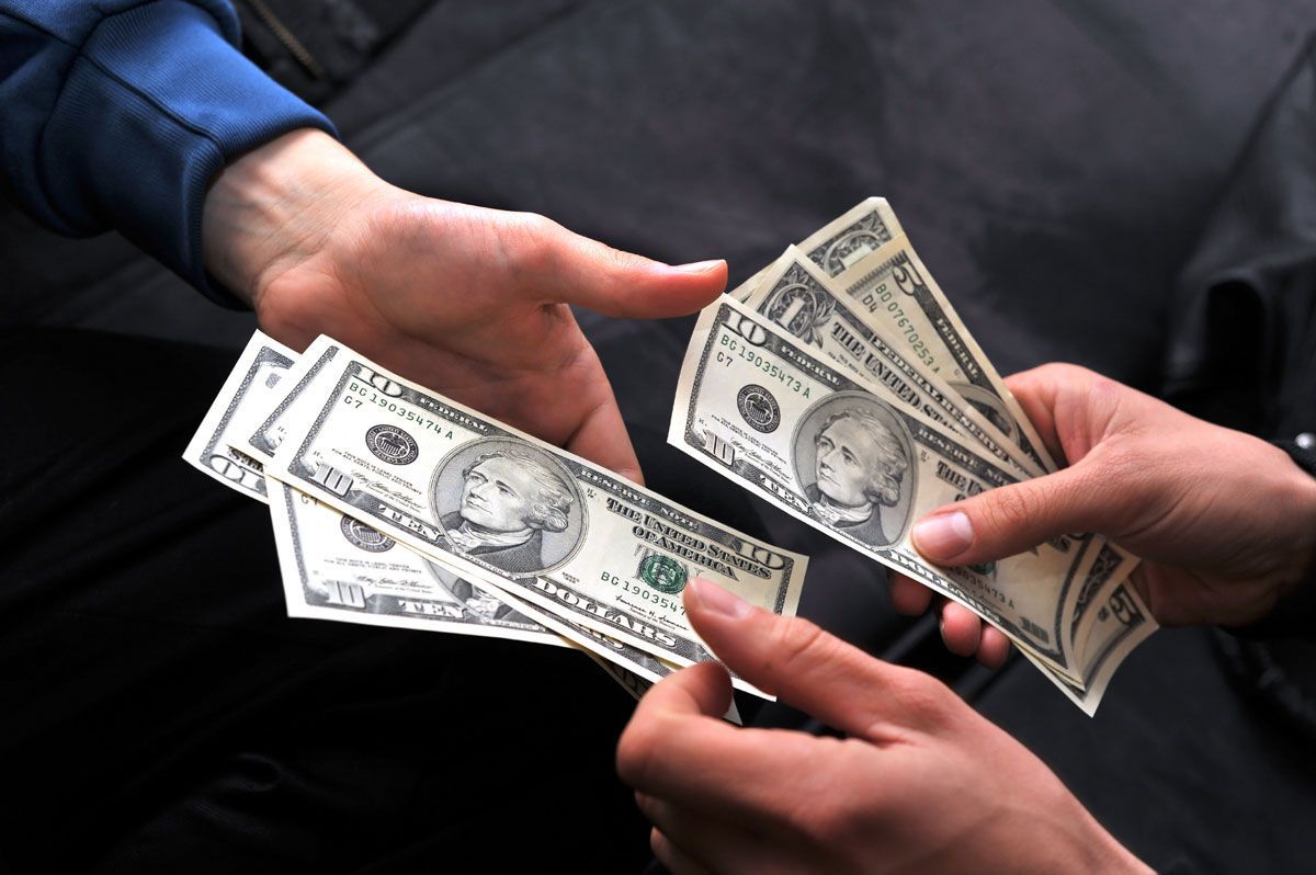 Hands exchanging U.S. dollar bills. One person offering money to another person.
