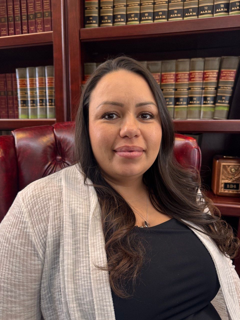 A professional portrait of a person sitting in a leather chair in front of a bookshelf filled with law books.