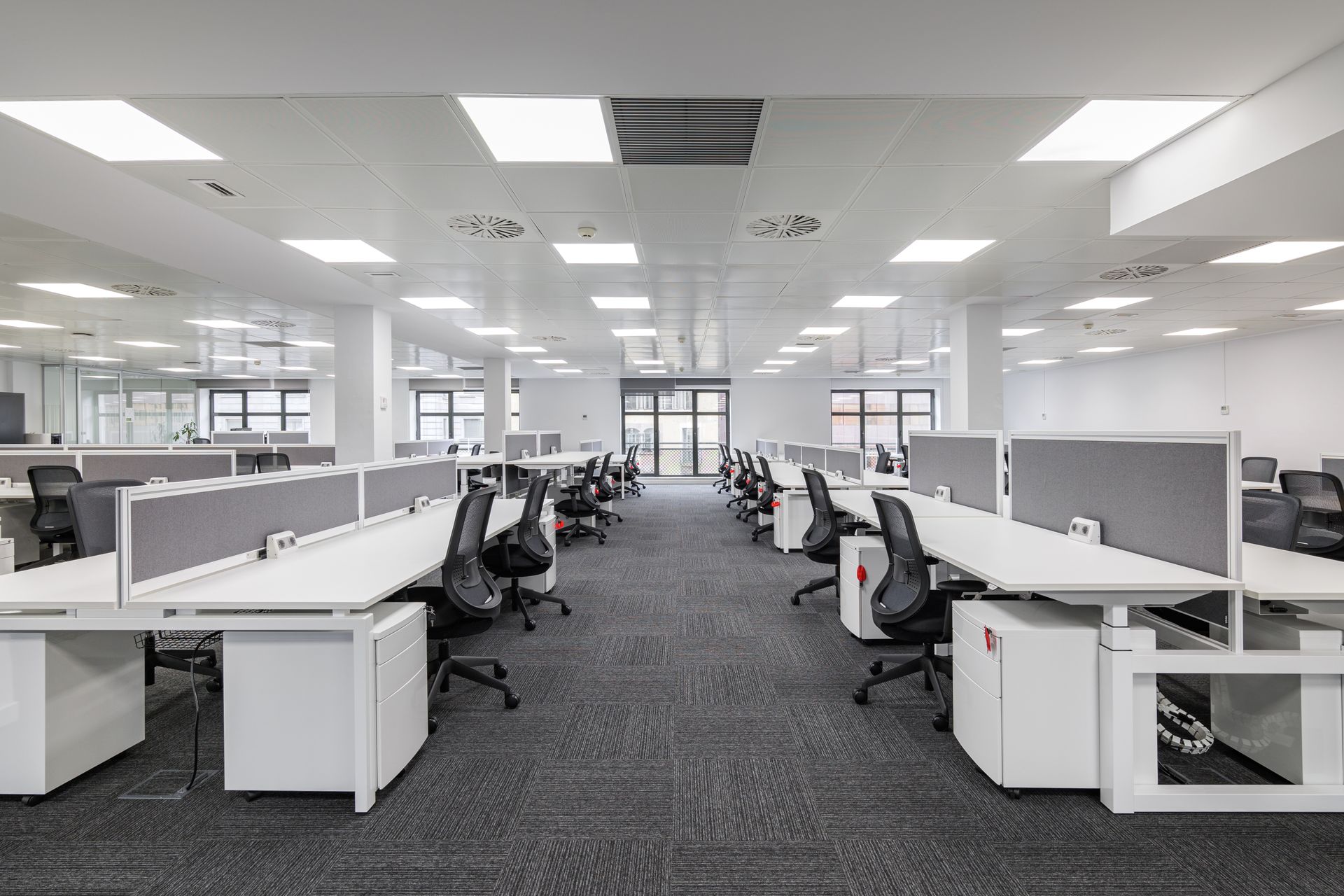 Modern open-plan office with rows of white workstations and black ergonomic task chairs Modern open-plan office with rows of white workstations and black ergonomic task chairs