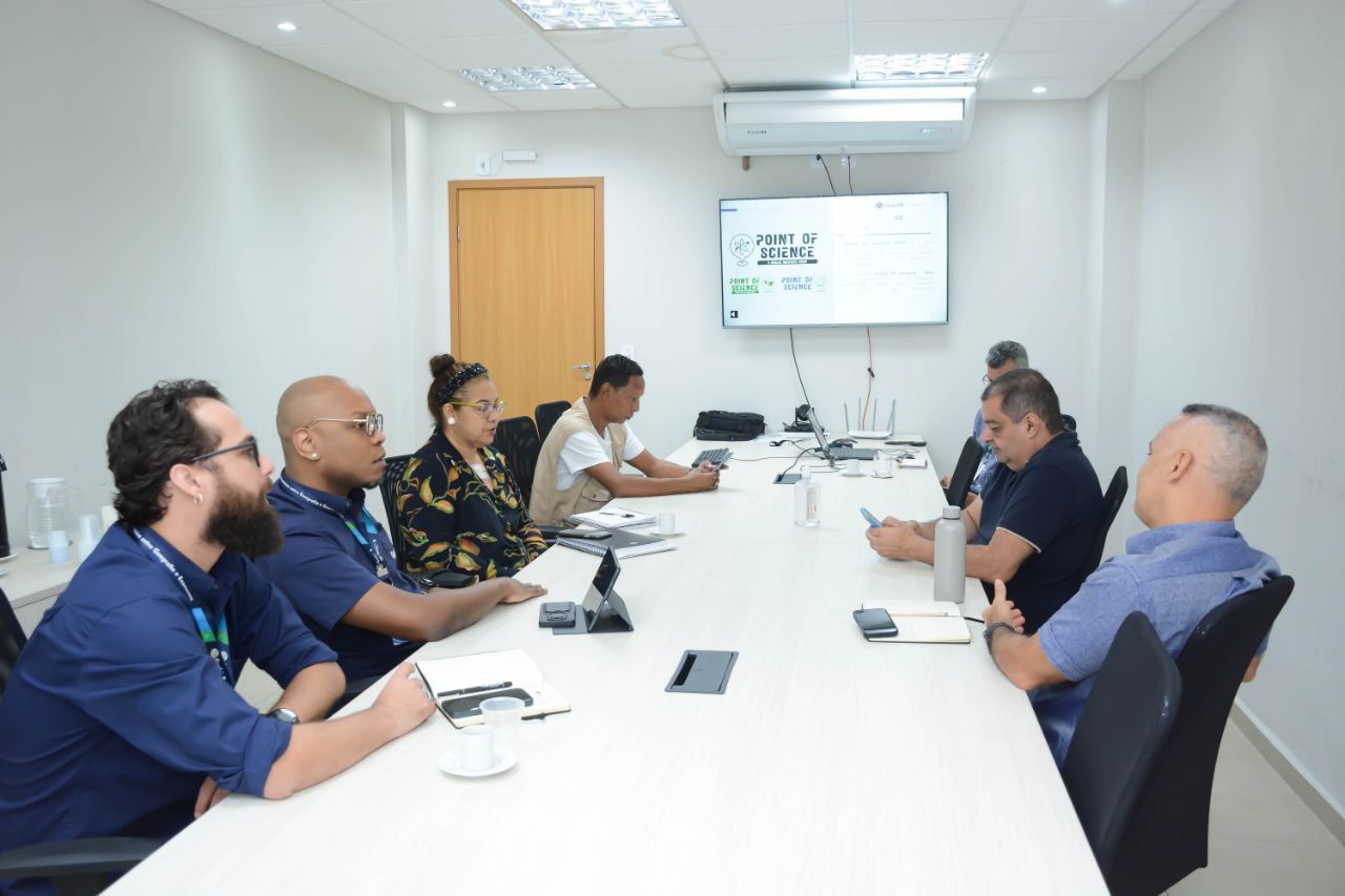 Um grupo de pessoas está sentado em uma longa mesa em uma sala de conferências.