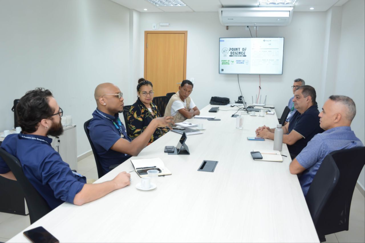 Um grupo de pessoas está sentado ao redor de uma longa mesa em uma sala de conferências.