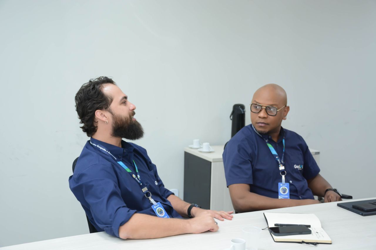 Dois homens estão sentados à mesa conversando entre si.