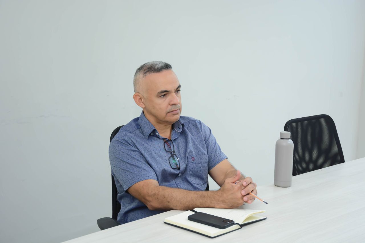 Um homem está sentado à mesa com um caderno e uma garrafa de água.