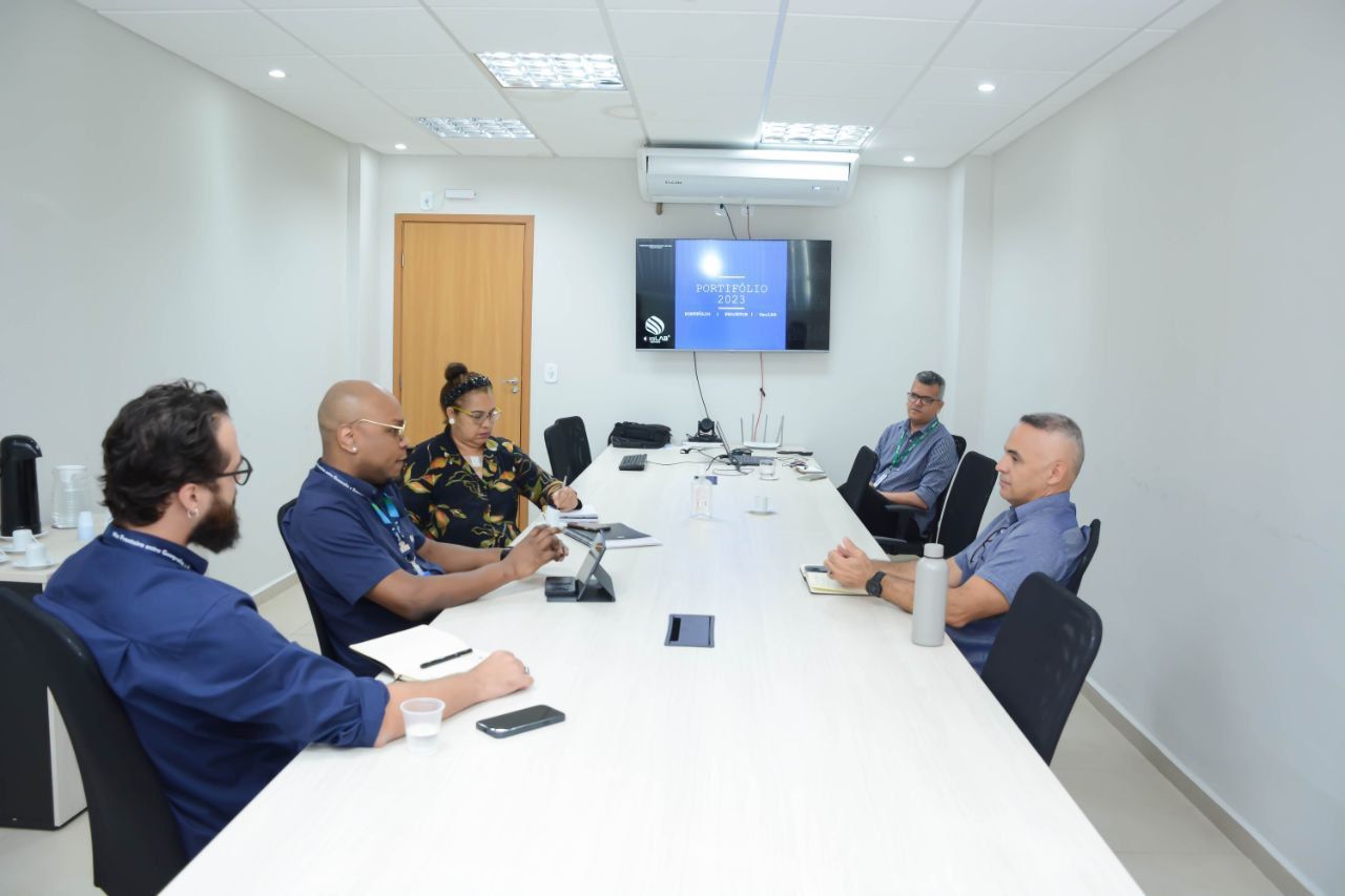 Um grupo de homens está sentado ao redor de uma longa mesa em uma sala de conferências.
