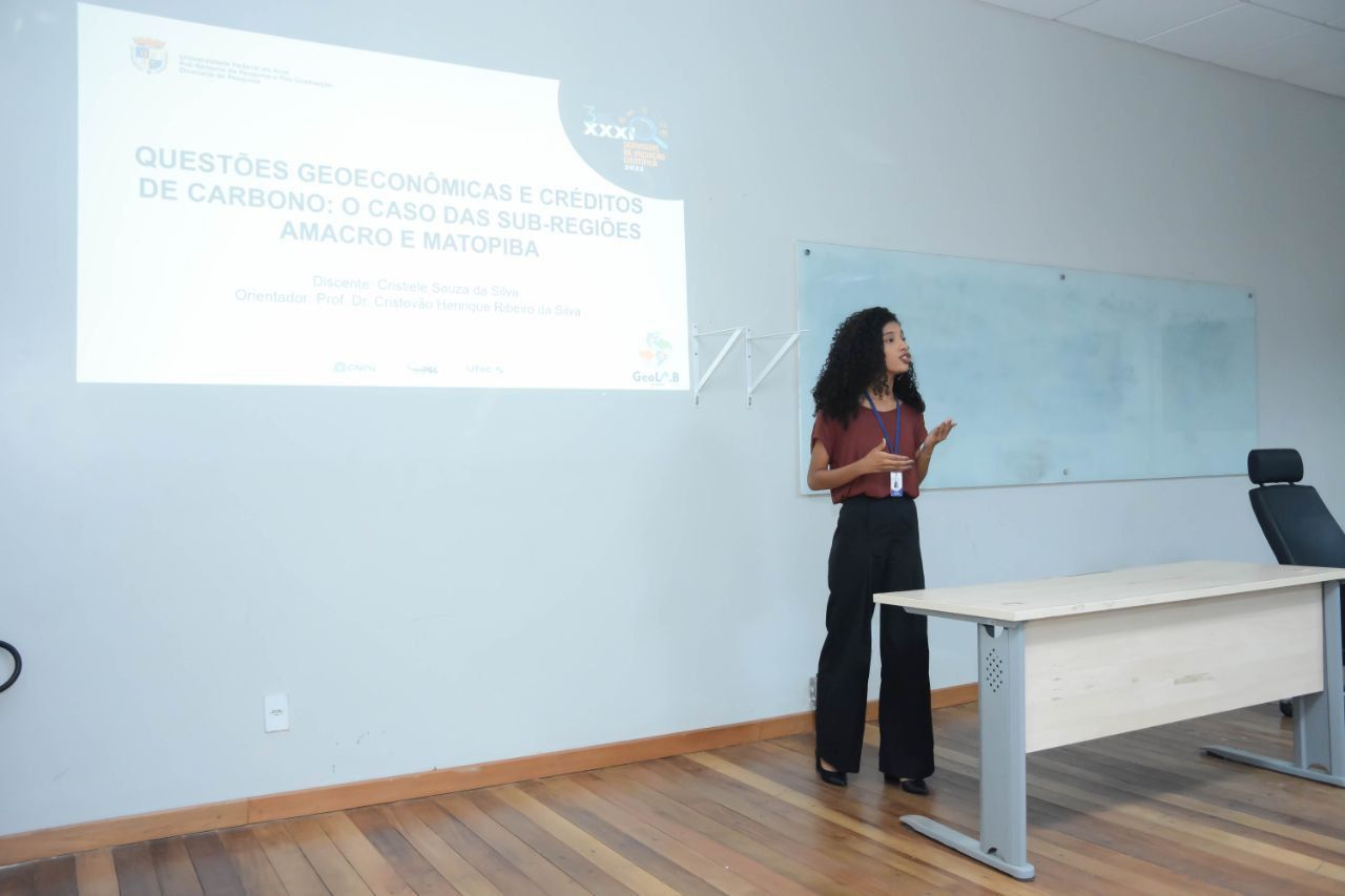 Uma mulher está fazendo uma apresentação em frente a uma tela de projetor em uma sala de aula.