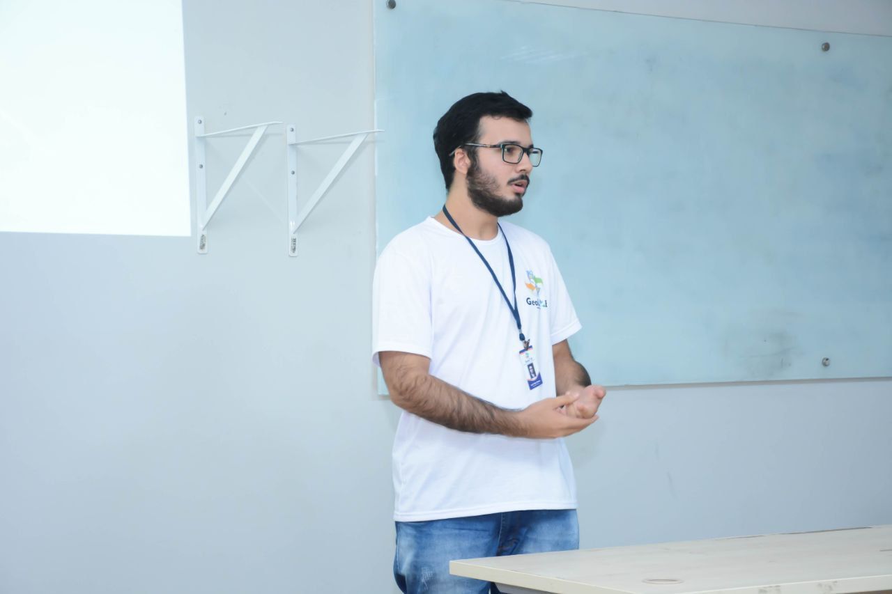 Um homem usando óculos e um cordão está parado em frente a um quadro branco.