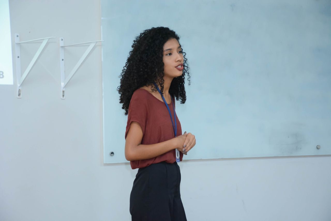 Uma mulher está fazendo uma apresentação em frente a um quadro branco em uma sala de aula.